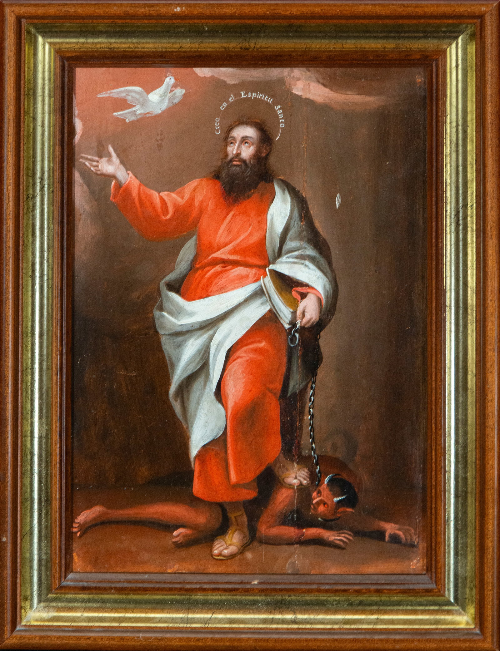 Saint Saturninus holding the devil. Spanish School. 18th-19th century.: Oil on panel. Measures 40 x 23 cm. The saint appears standing, dressed in a red tunic and white cloak, holding a book and a chain that binds the demon beneath his feet. The inscription 'Believe in the