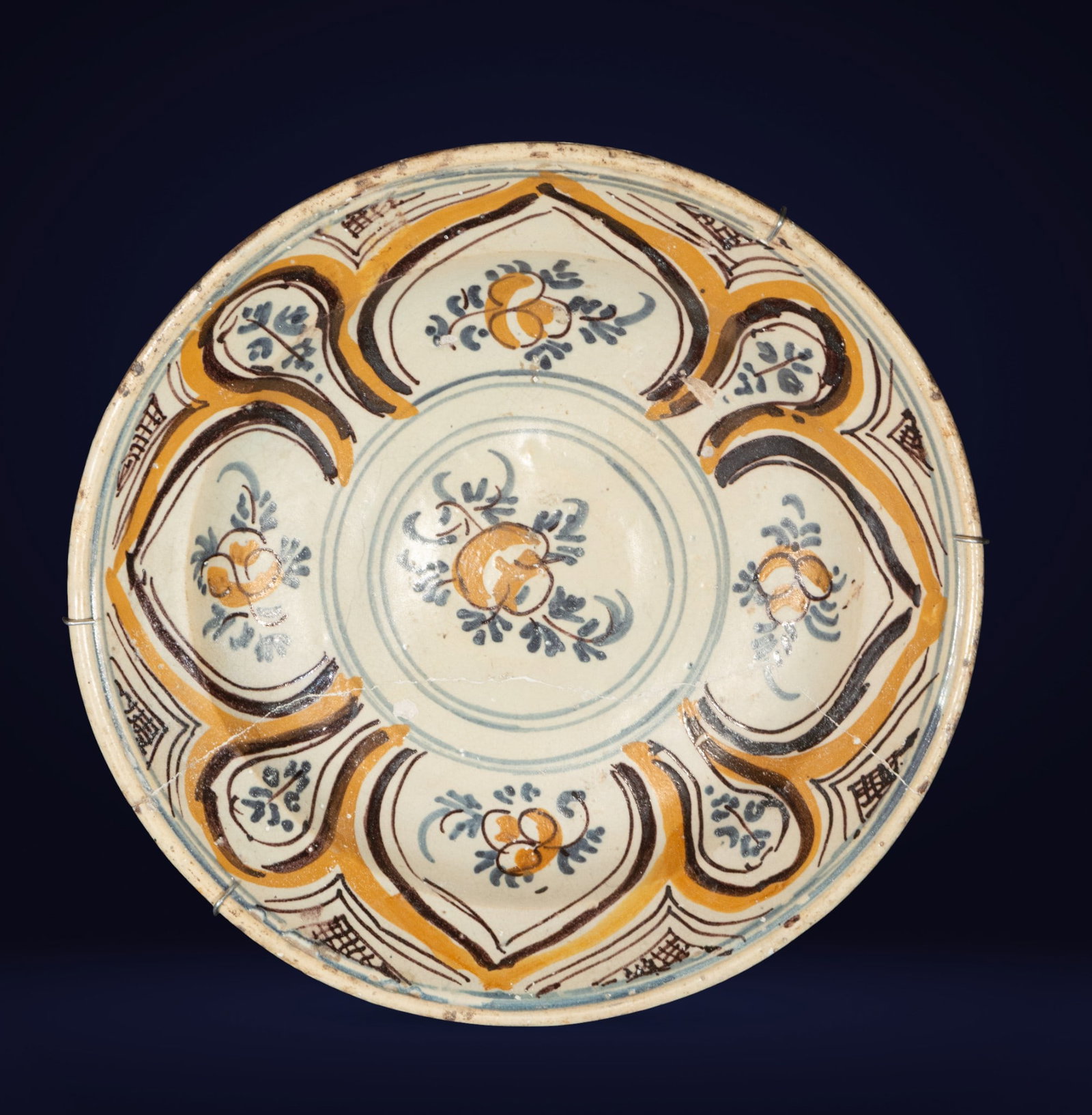 Triana plate with Hispano-Arabic decoration. Spanish School. 18th century.: Glazed ceramic in ochre, blue, and green tones. Measures 34 x 34 x 6 cm. Design features lobed reserves and floral elements. The mix of colors and strokes evokes the enduring Andalusian legacy in 18th