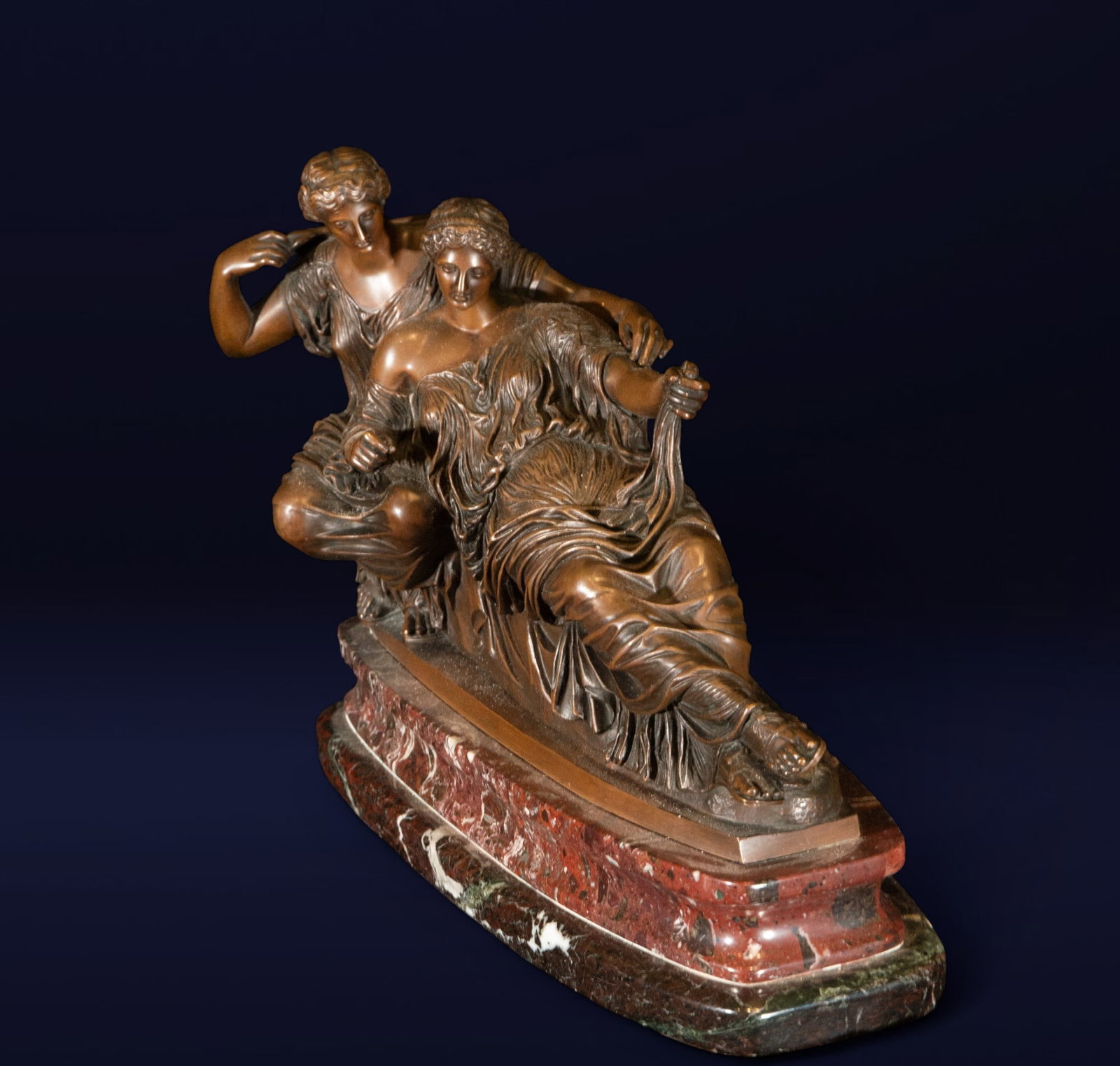 Sculptural group of reclining nymphs. French school. 19th century.: Patinated bronze on a red marble base. Dimensiones 28 × 36 × 12 cm. The group depicts two female figures in classical tunics, one reclining languidly and the other in a protective pose, creating a d