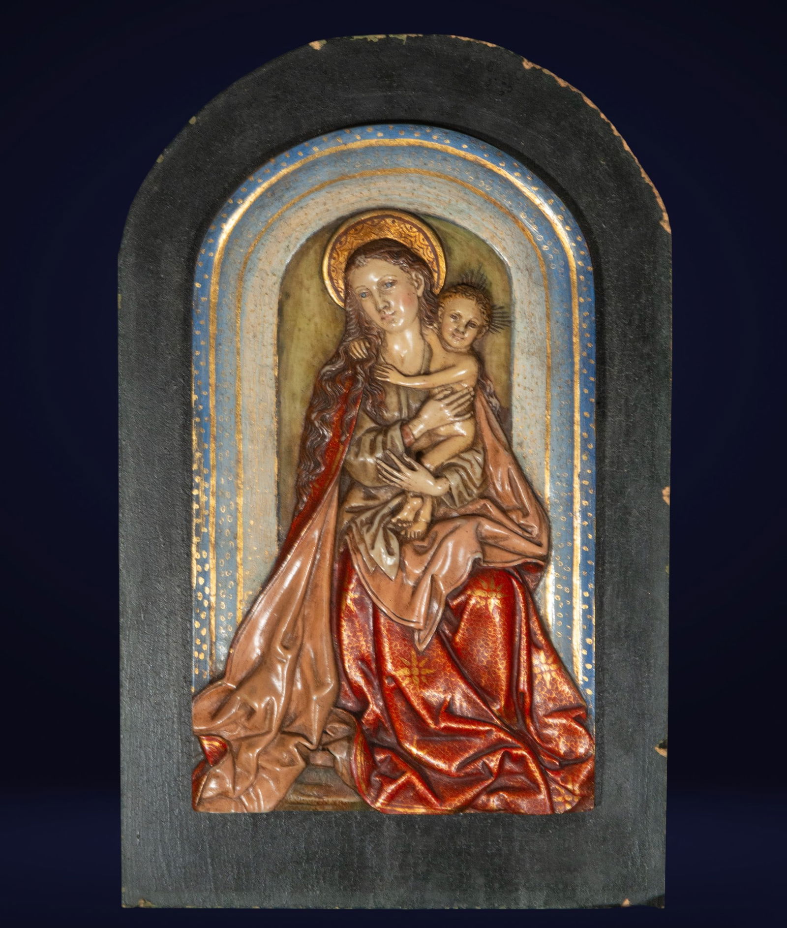 Alabaster relief of the Virgin and Child. Neo-Gothic School. 19th century: Polychrome alabaster on a wooden background. This delicate sculptural composition depicts the Virgin Mary in a serene attitude, tenderly holding the Child Jesus. The relief stands out for its brillian
