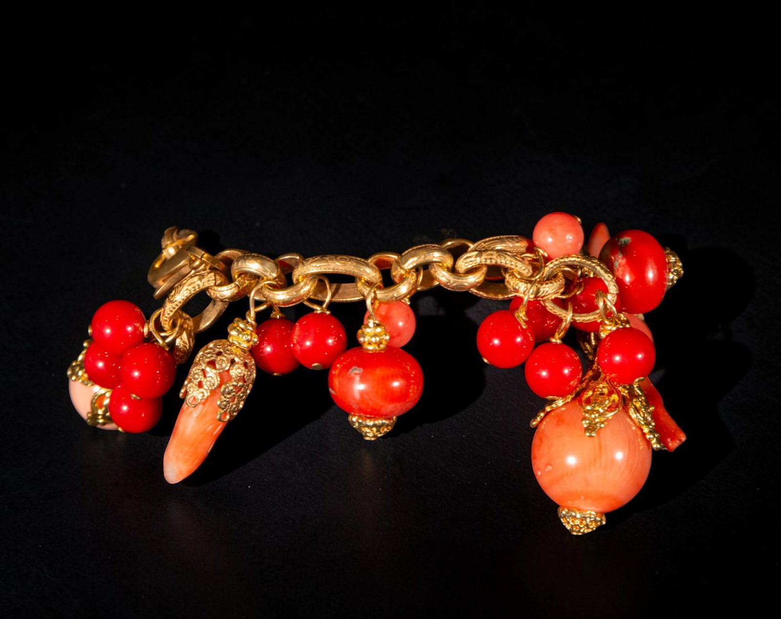 Bracelet in gold-plated silver and coral: Gold-plated silver and coral bracelet. Made with a thick link chain and decorated with numerous coral pendants in shades of red and pink, in spherical, oval, and elongated shapes, all enhanced with