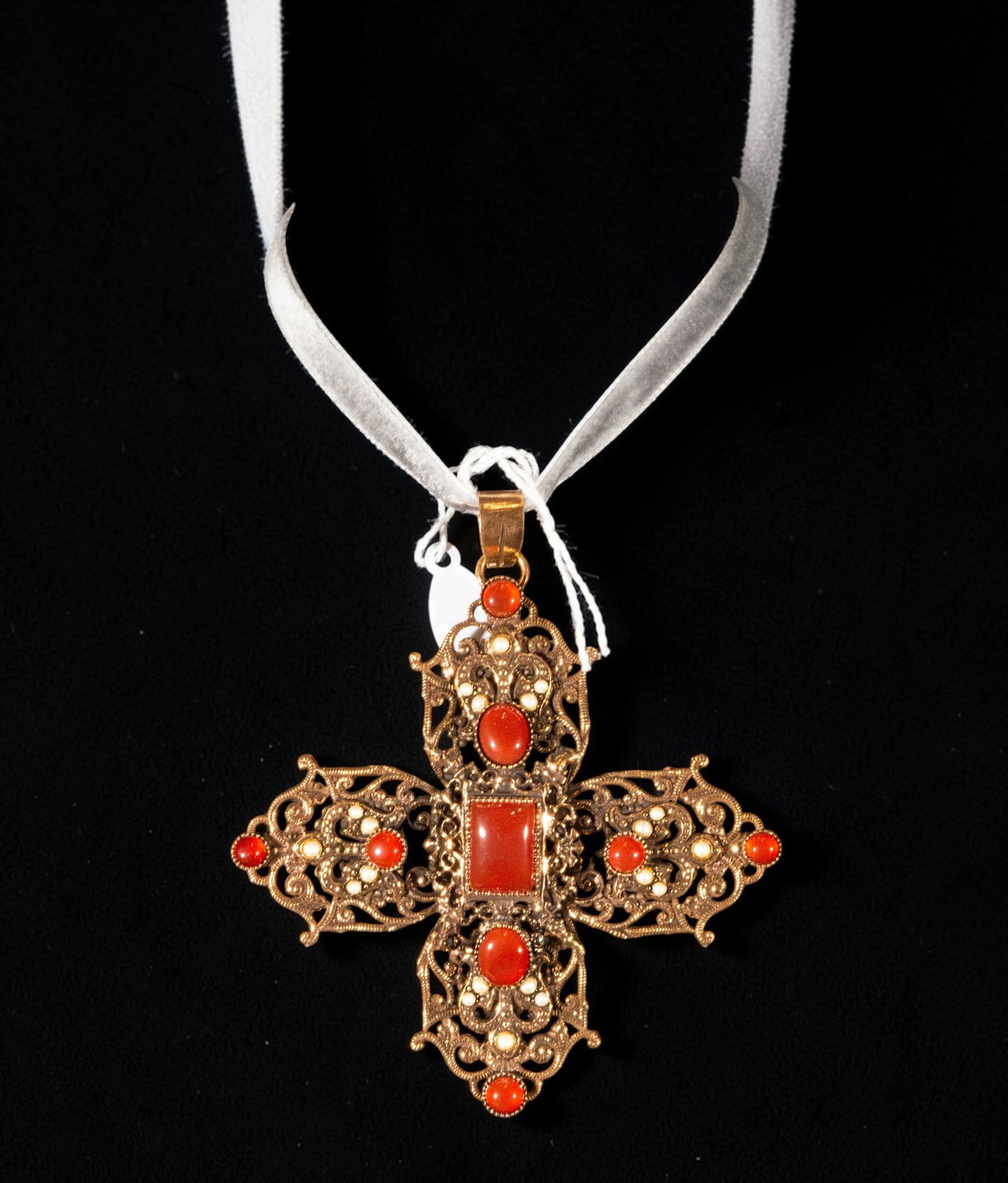 Silver-gilt cross with carnelian and pearls: A gilt silver cross with carnelian and pearls. Crafted with an openwork structure and flared arms, it incorporates cabochons and carnelian plaques in a reddish hue, accompanied by small pearls