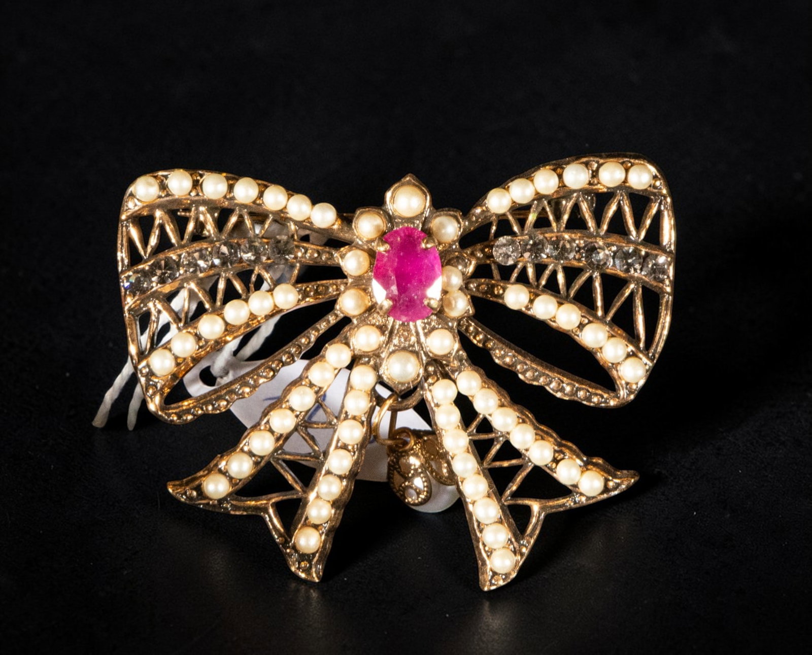 Gold-plated silver brooch with zircon pearls and synthetic ruby: A silver-gilt brooch with zirconia pearls and a synthetic ruby. Crafted in the shape of a large bow, it features an openwork structure decorated with small pearls and zirconias, arranged around a