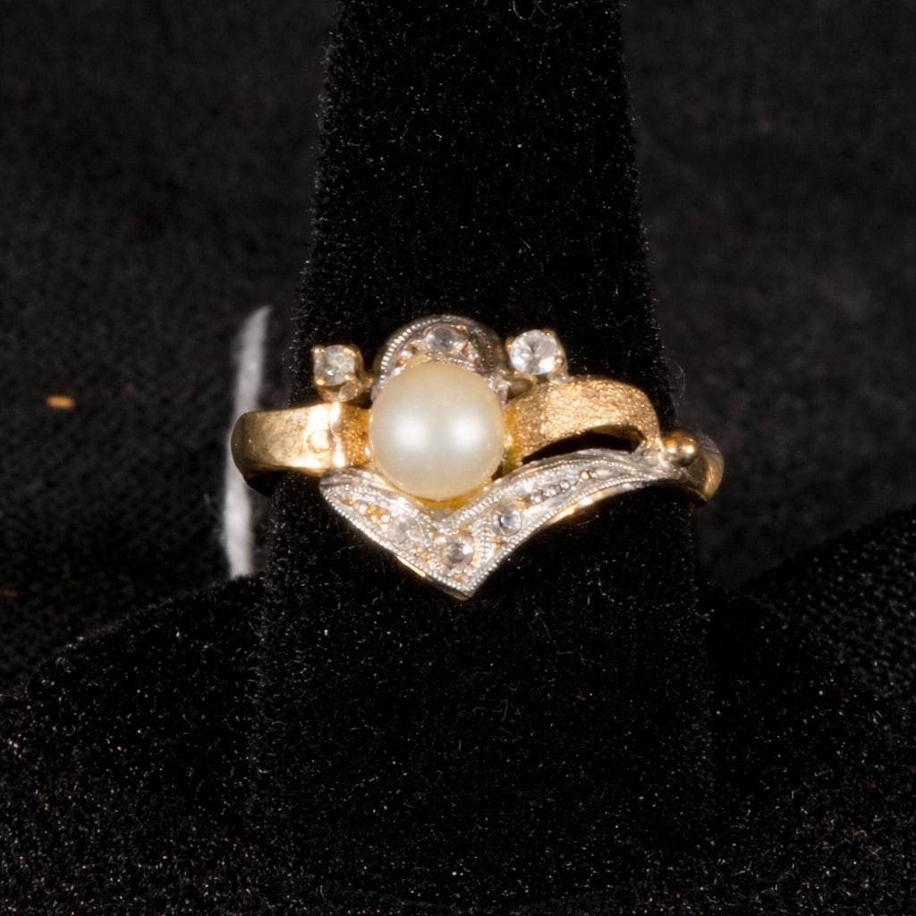 Gold pearl ring: Pearl gold ring. Designed with a gold band and a central motif featuring a pearl, it incorporates small, sparkling elements that complement the setting and a curved lower band decorated with light-col