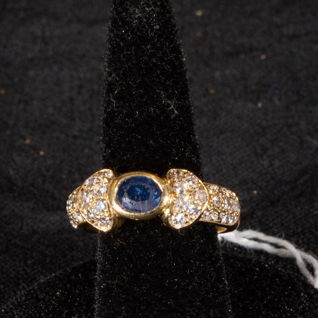 18k matte gold ring with oval-cut sapphire center and brilliant-cut diamonds, weight 7.70: 18k matte gold ring with an oval-cut sapphire center stone and brilliant-cut diamonds, weight 7.70g. The piece features an oval sapphire in the center, set in a bezel and flanked by areas decorated wi