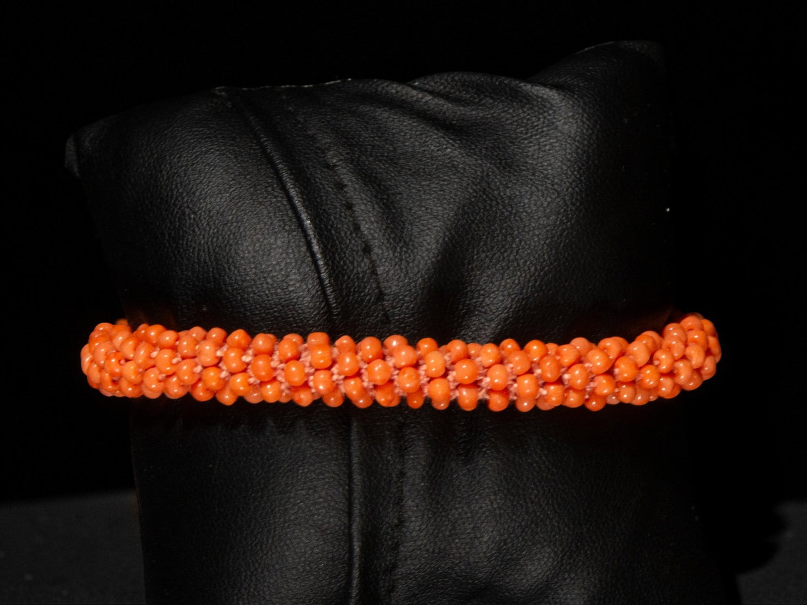 Coral bracelet: A coral bracelet composed of small orange beads arranged in a braided, tubular structure. The continuous, flexible arrangement creates a uniform and organic profile. The bead weave forms a delicate, r
