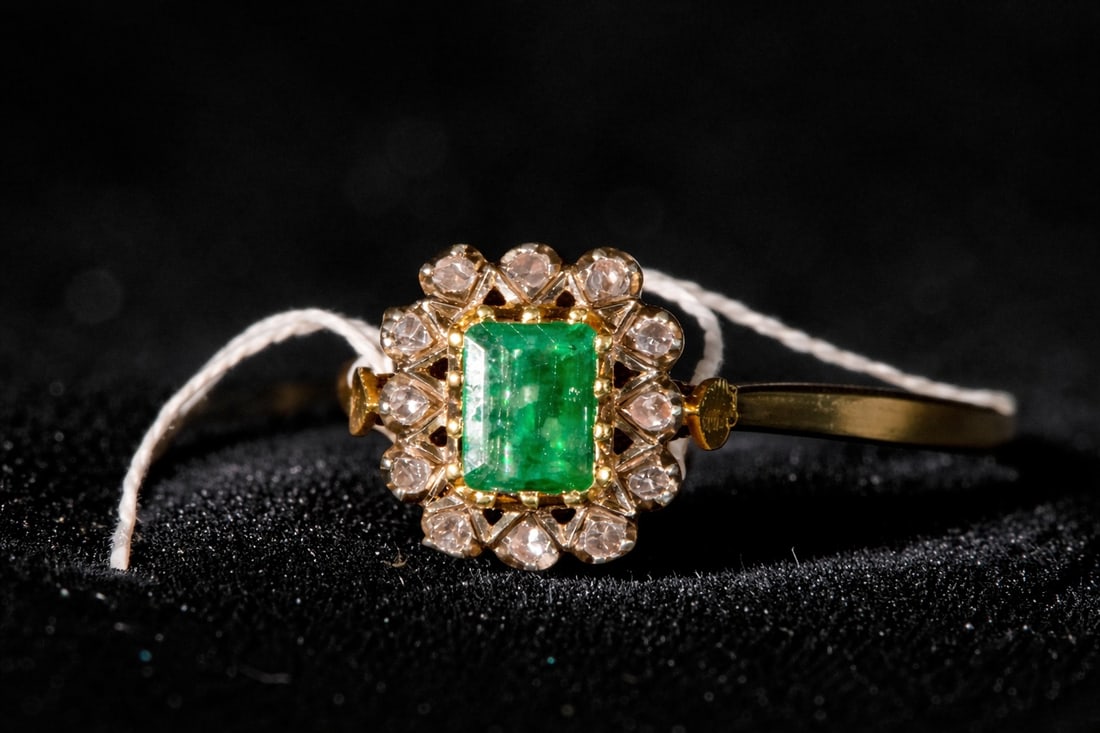 Antique yellow gold ring with brilliant-cut diamonds and a central emerald: Antique yellow gold ring with brilliant-cut diamonds and a central emerald. The piece features a smooth band that elevates a vertically oriented motif, arranged around a rectangular-cut emerald and fl