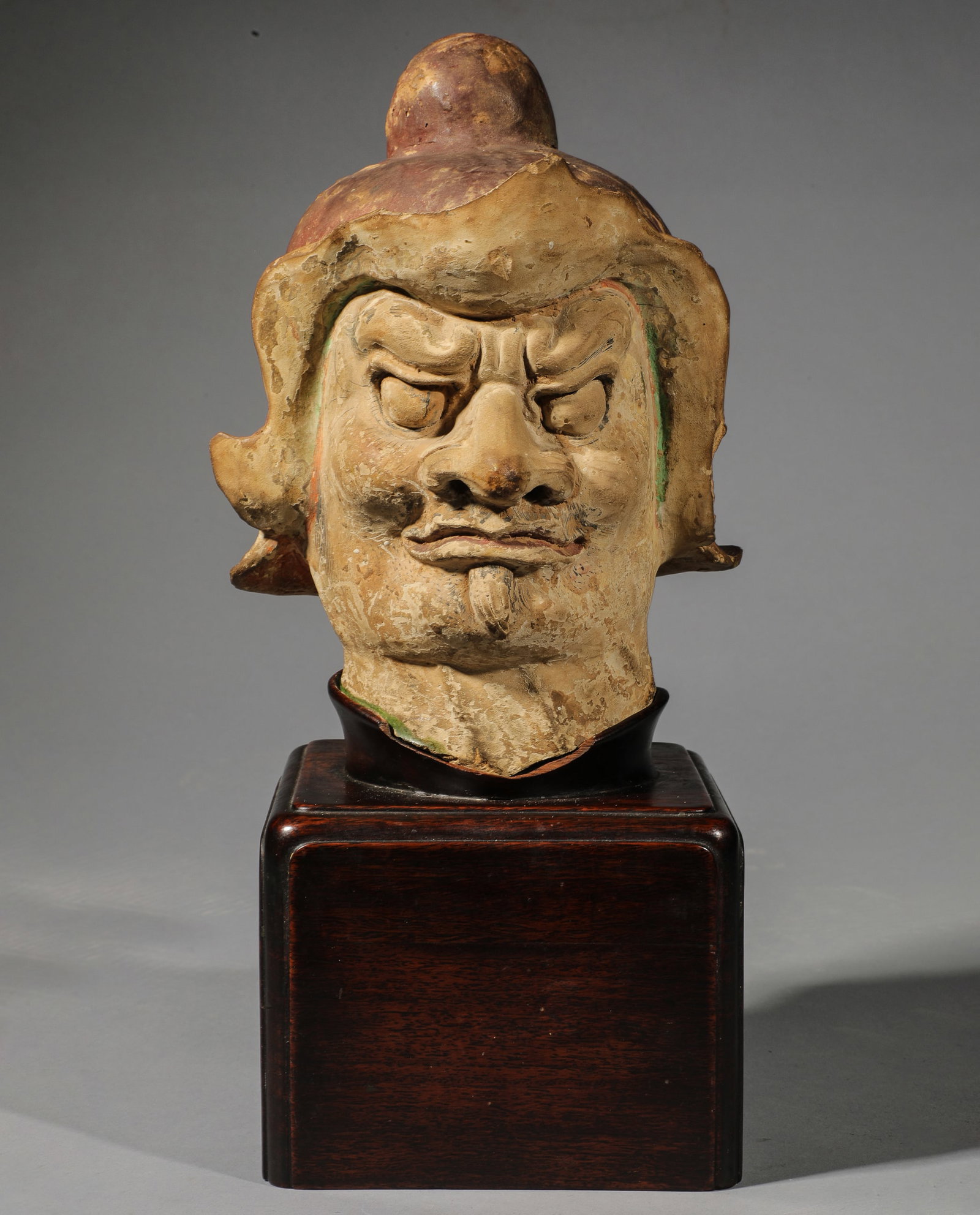 Large Tang Archaic Chinese head of Lokapala, a tomb guardian, with a fierce expression and wearing a: Large Tang Dynasty Chinese Archaic Head of Lokapala, guardian of a tomb, with a fierce expression and wearing a cap. Terracotta. Traces of polychromy. China. Tang Dynasty (618-907). 21 cm. Lot in inte