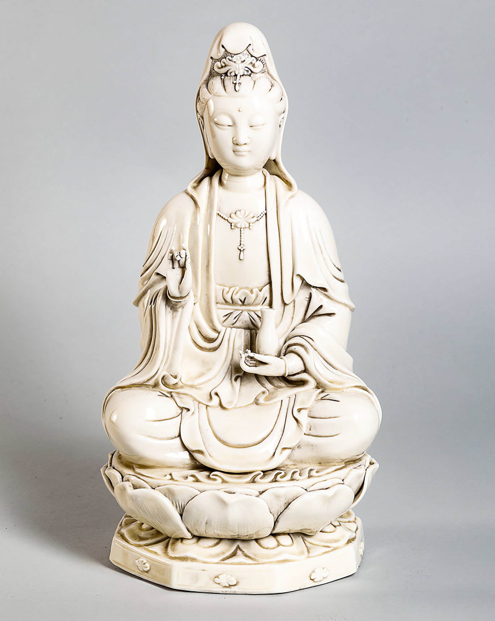 Guanyin seated in meditation on a lotus-shaped base with a double row of petals, dressed in a: The Bodhisattva Kwan Yin sits in meditation on a lotiform base with a double row of petals, dressed in a bubbly-pleated monastic robe, adorned with a jeweled breastplate, and wearing a jeweled bun. He