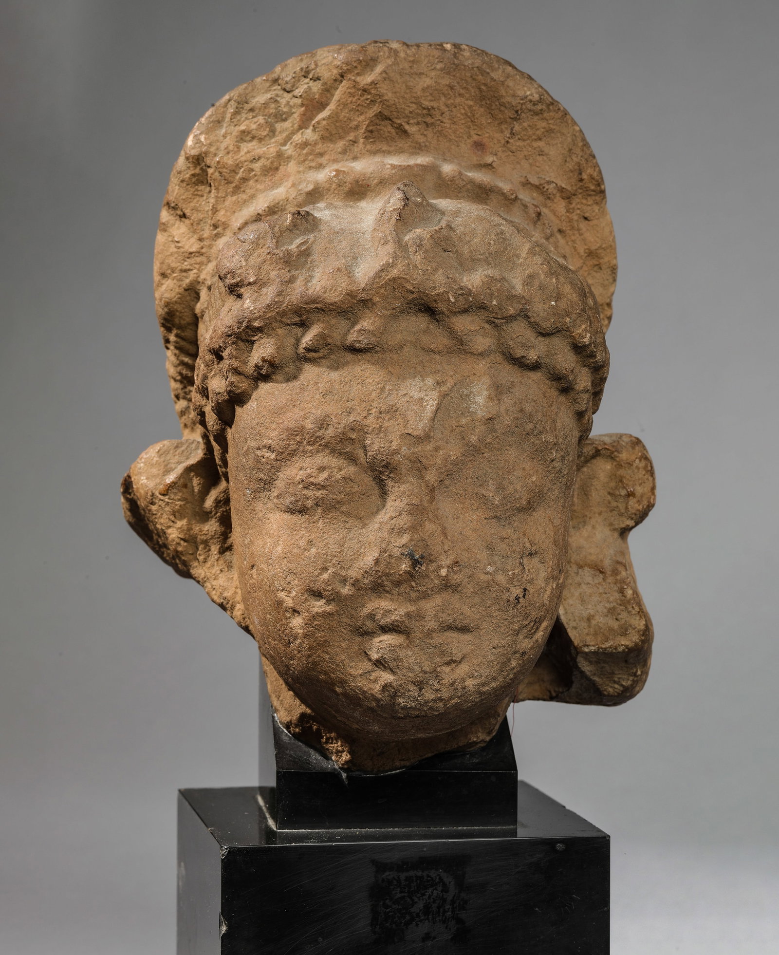 Head of a female deity with a bun. Beige sandstone with a patina of age. India, Gupta Dynasty. 3rd: Head of a female deity with a bun. Beige sandstone with a patina of age. India, Gupta Dynasty. 3rd to 5th century AD. Significant erosion and chipping. Height 22 cm. Lot in international warehouse (ou