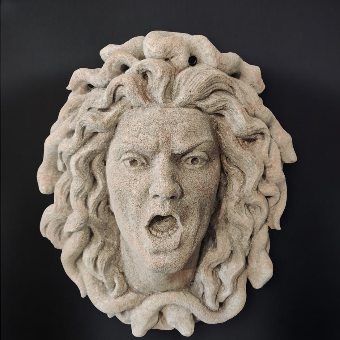 Stone figurehead from Vicenza representing Medusa, Italy, 20th century: Carved Vicenza stone. Dimensions: 46 × 37 × 20 cm. An imposing mask representing Medusa, the mythological female figure with snakes in her hair, a symbol of power and protection. Sculpted with great