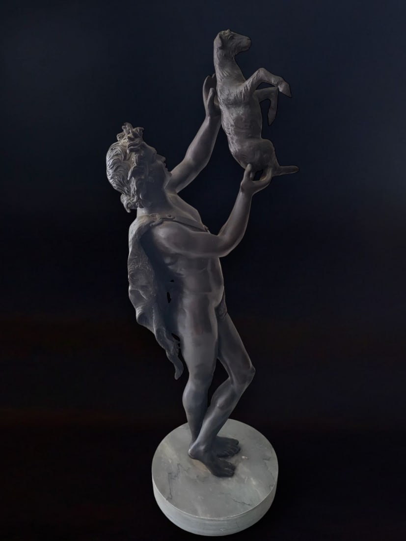 Bronze sculpture depicting a satyr with a goat in his arms, Italy, 20th century: Patinated bronze. Dimensions: 68 × 20 cm. Magnificent sculpture inspired by classical themes of Greek and Roman art, where satyrs and fauns—minor deities with both human and animal features—were 