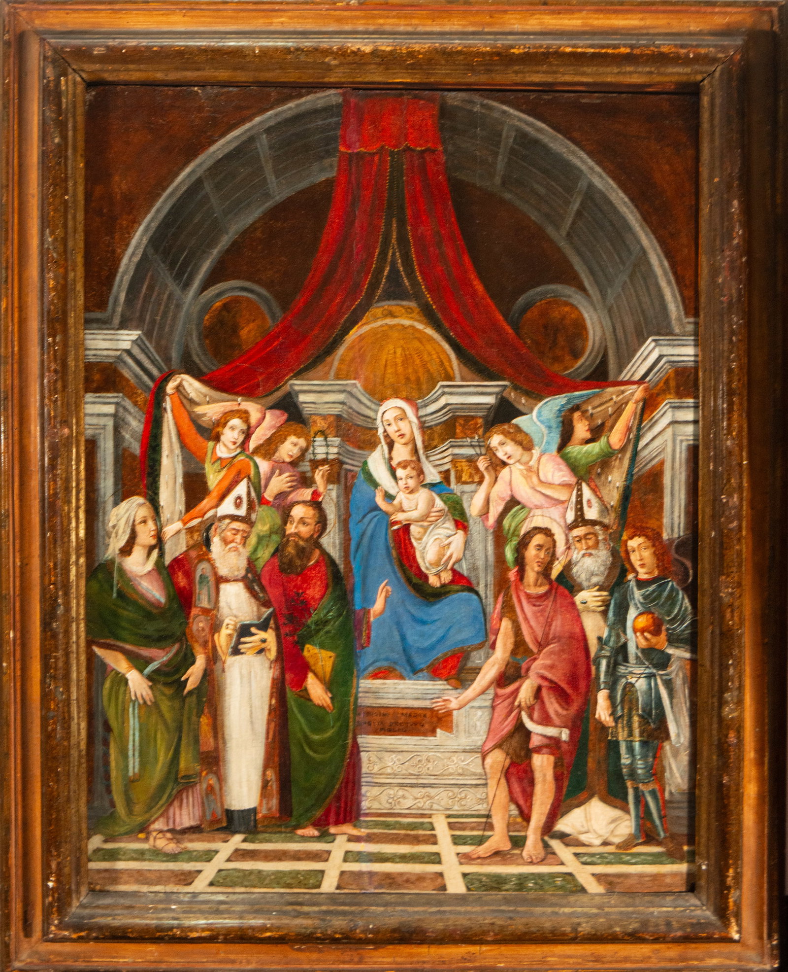 Virgin and Child enthroned with saints, Spanish School, 16th Century: Oil on panel. Dimensions 67 x 50 / 82 x 64 cm. A sacred scene set in a Renaissance-style architectural interior, with the Virgin and Child enthroned beneath a canopy, surrounded by saints in a symmetr