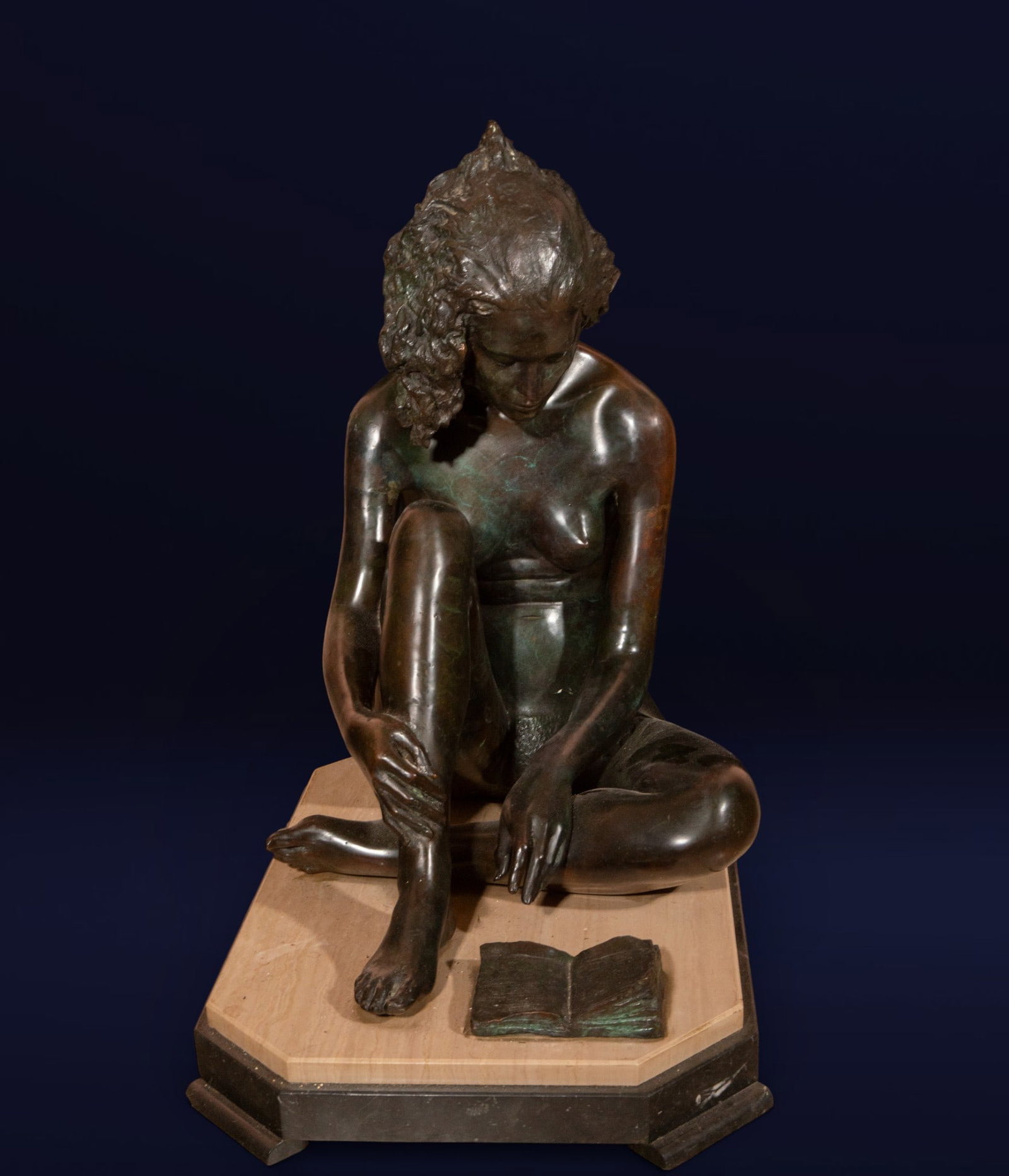 Female figure seated with a book, European School, 20th century: Patinated bronze. Dimensions: 70 x 44 x 70 cm. Seated nude female figure in an introspective pose, with one leg bent and her head slightly inclined towards an open book at her feet. The composition is