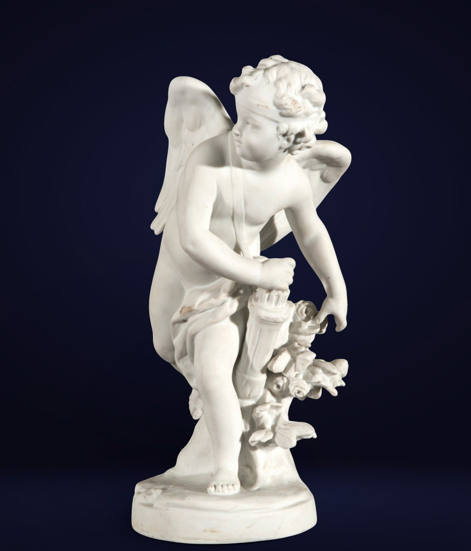 Decorative Cupid in French biscuit porcelain - 19th Century: White porcelain. Measures 26 x 12 x 18 cm. Figure of a winged putto in a dynamic pose, with a nude body slightly turned and accompanied by a quiver, torch, and floral garland—elements that allude to