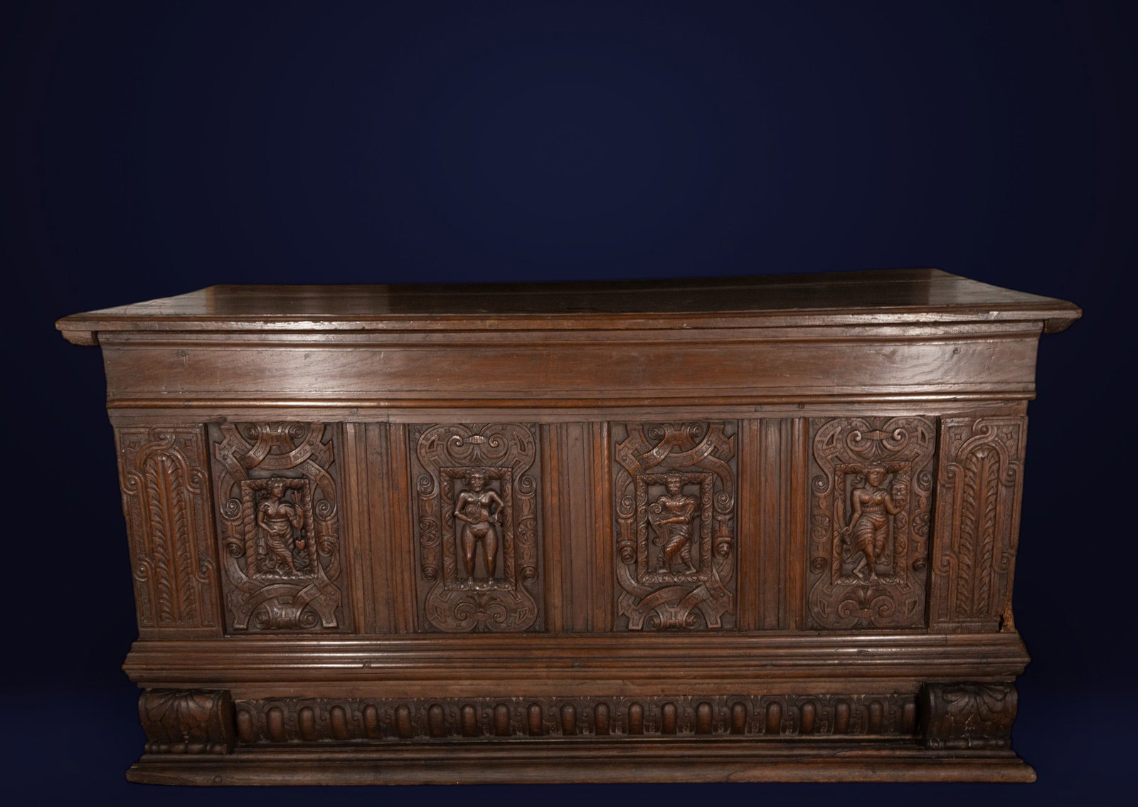 Large Italian chest, Veneto, 17th century: Carved wood. Dimensions: 82 x 163 x 70 cm. Large chest with a richly carved front featuring figurative panels and grotesque ornamentation, arranged in a rhythmic composition of pilasters, moldings, an
