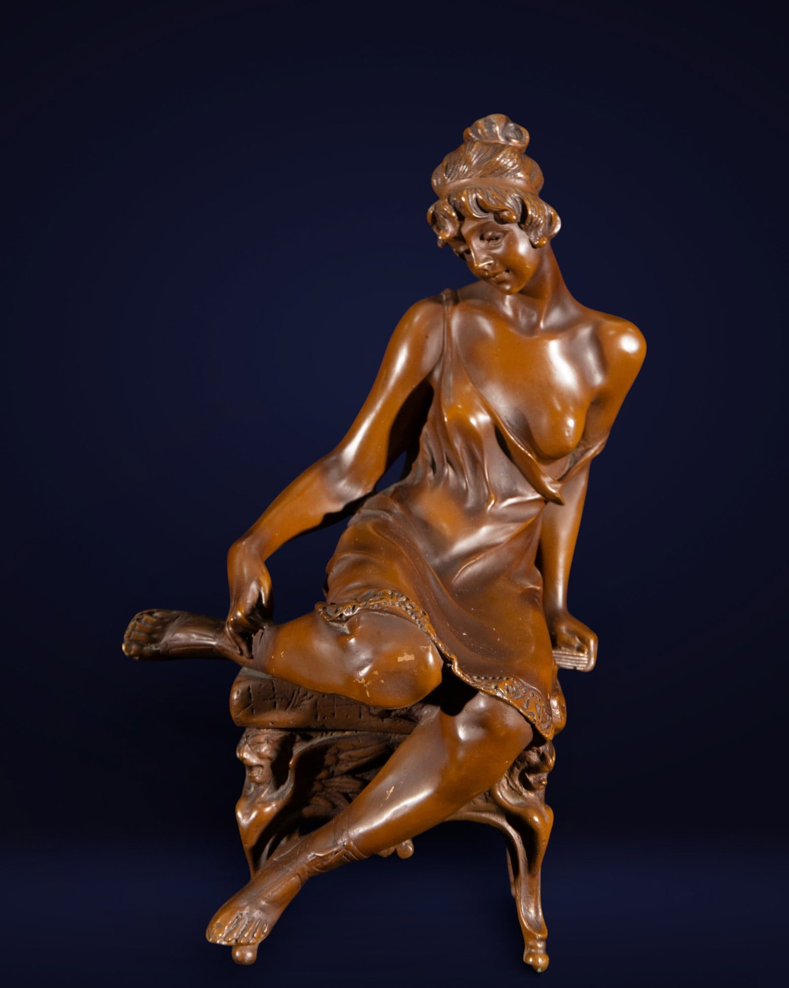 Seated female figure, Art Deco style, 20th century: Patinated bronze. Measures 41 x 21 x 22 cm. Sculpture of a semi-nude female figure seated with a languid and elegant pose on a chair with a curved profile. The gentle twist of the body, the drape of t