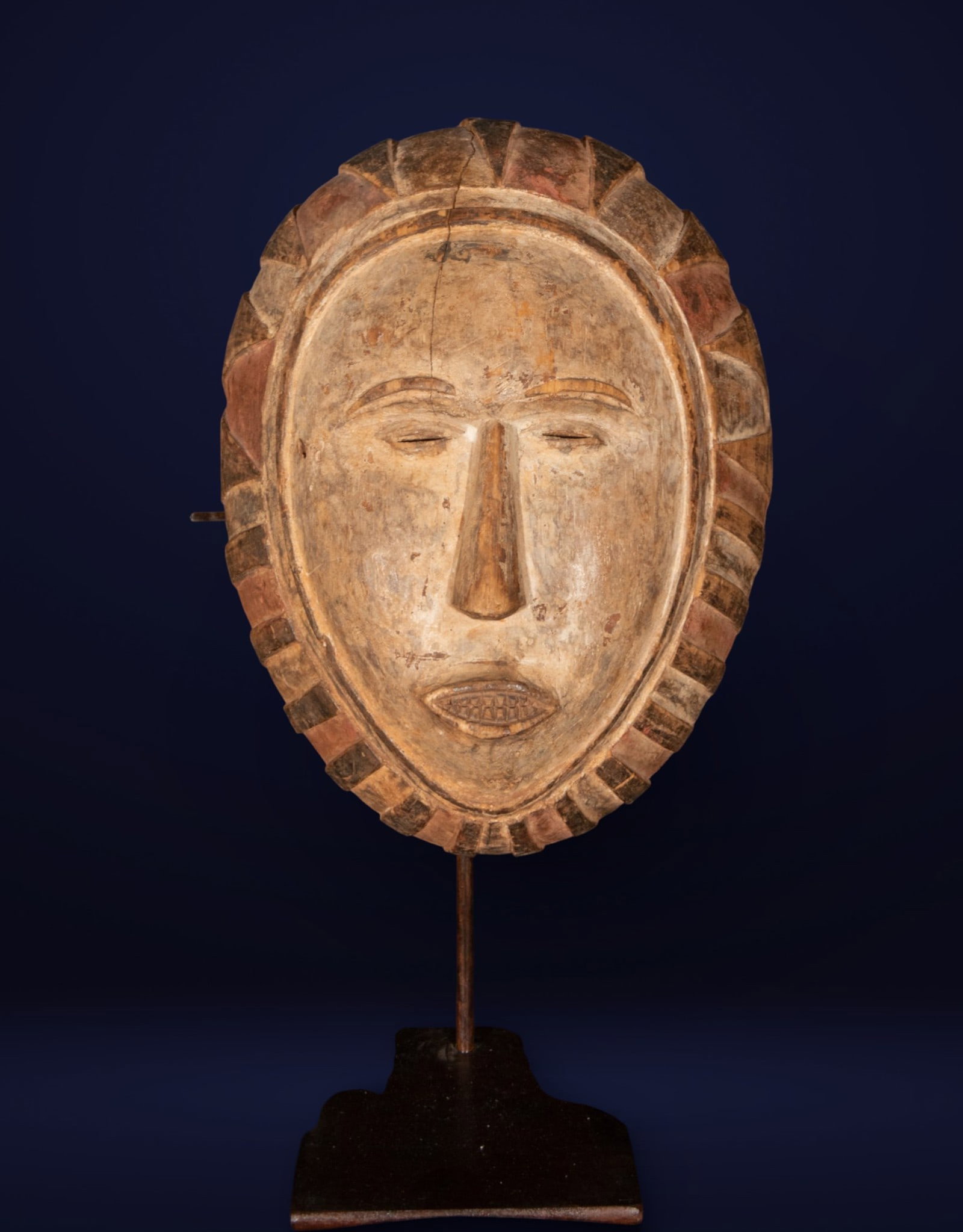 African mask, possibly Fang area, Central Africa, 20th century: Carved wood with traces of polychromy. Measures 46 x 27 x 25 cm. Mask with an oval face and stylized features, a long straight nose, half-closed eyes, and a small mouth with prominent teeth, surrounde