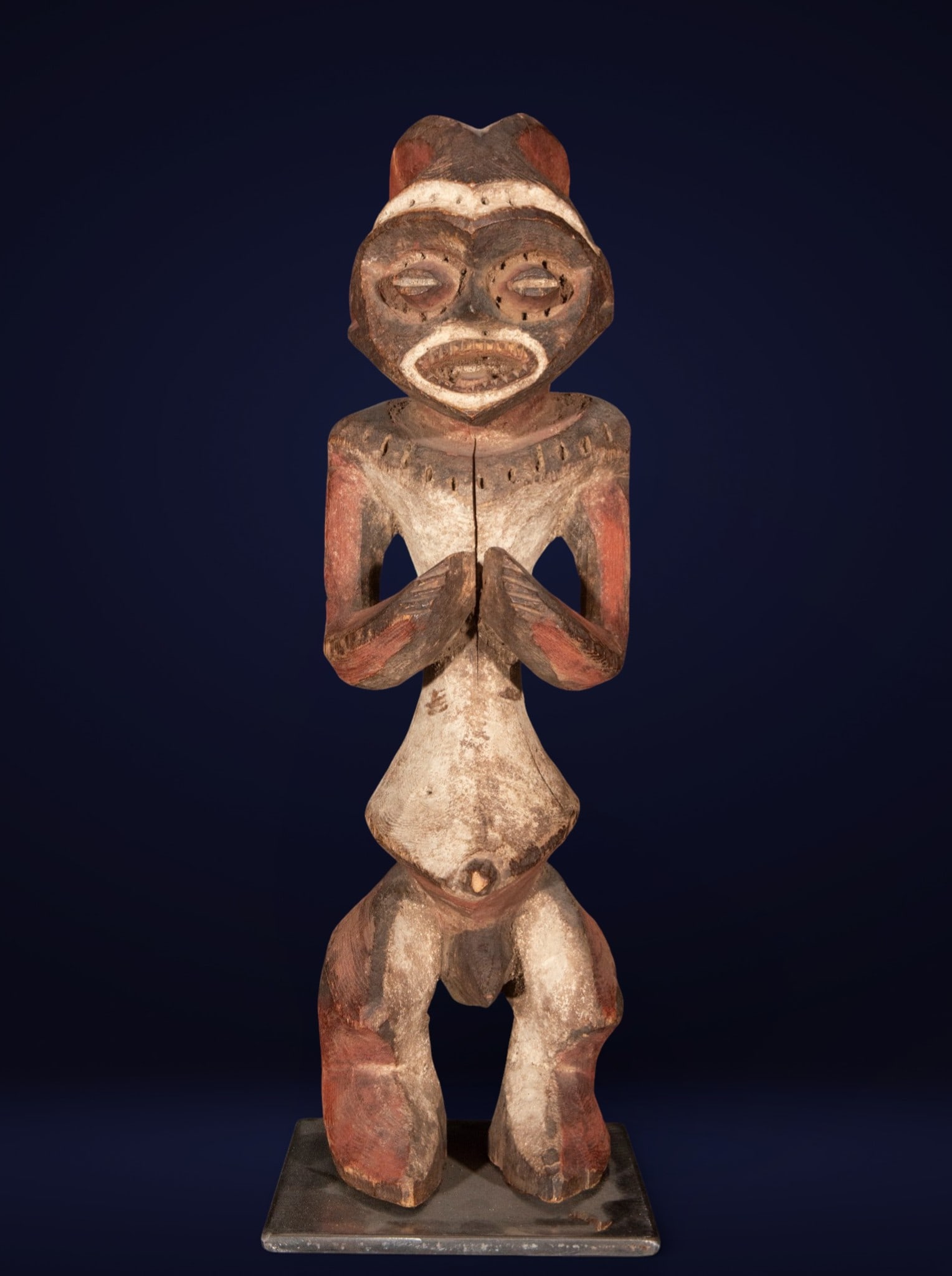 African tribal figure, African school, 20th century: Carved wood with traces of polychromy. Measures 47 x 15 x 15 cm. Standing anthropomorphic figure with hands clasped on its chest, head with large almond-shaped eyes and an open mouth, rendered in a sc