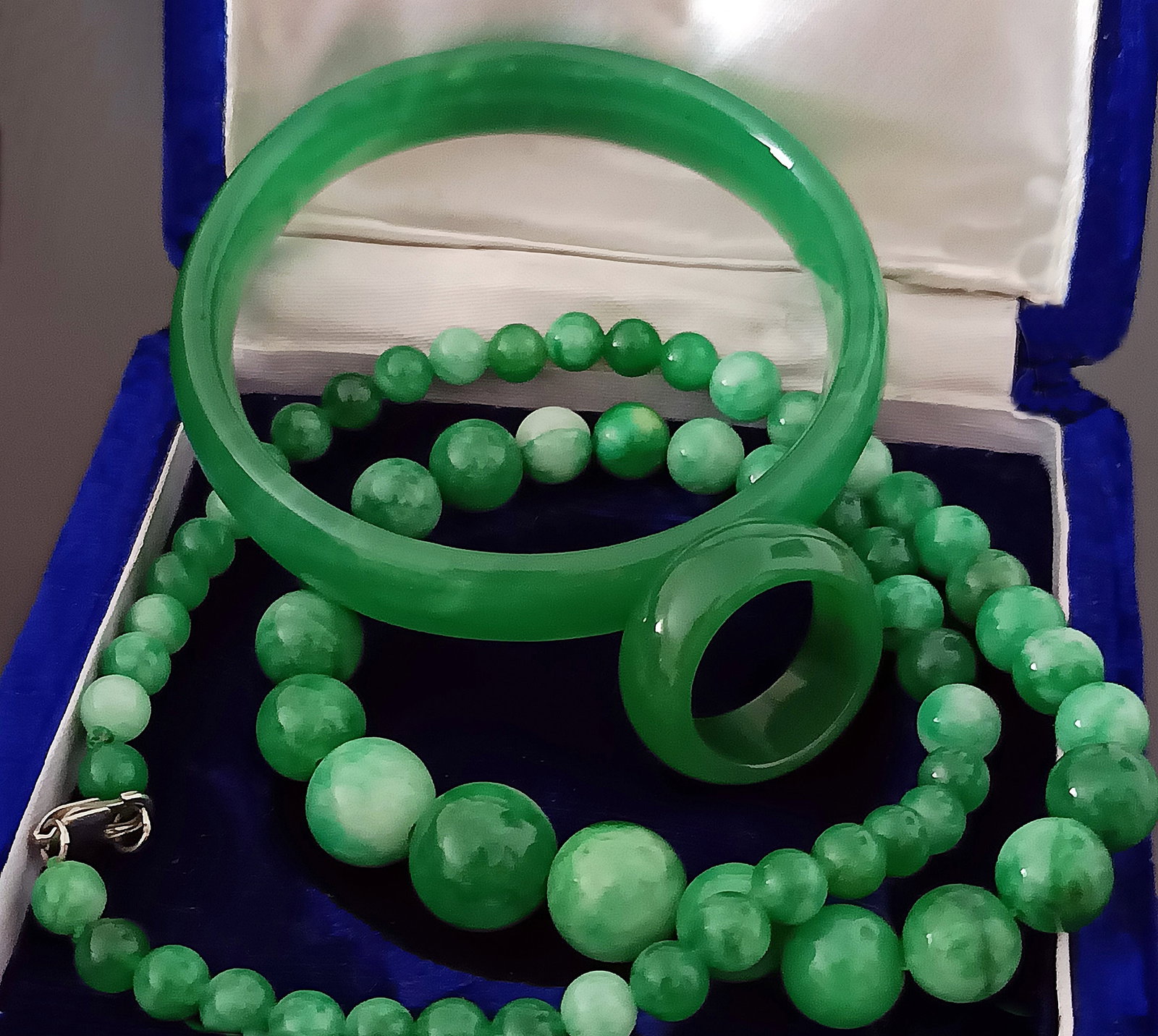 Vintage lot of natural emerald green jade consisting of a necklace, bracelet and ring, total weight: Elegant vintage set crafted from natural emerald green jade, comprising a necklace of graduated spherical beads, a rigid bracelet with a circular profile, and a matching ring. The pieces feature an at