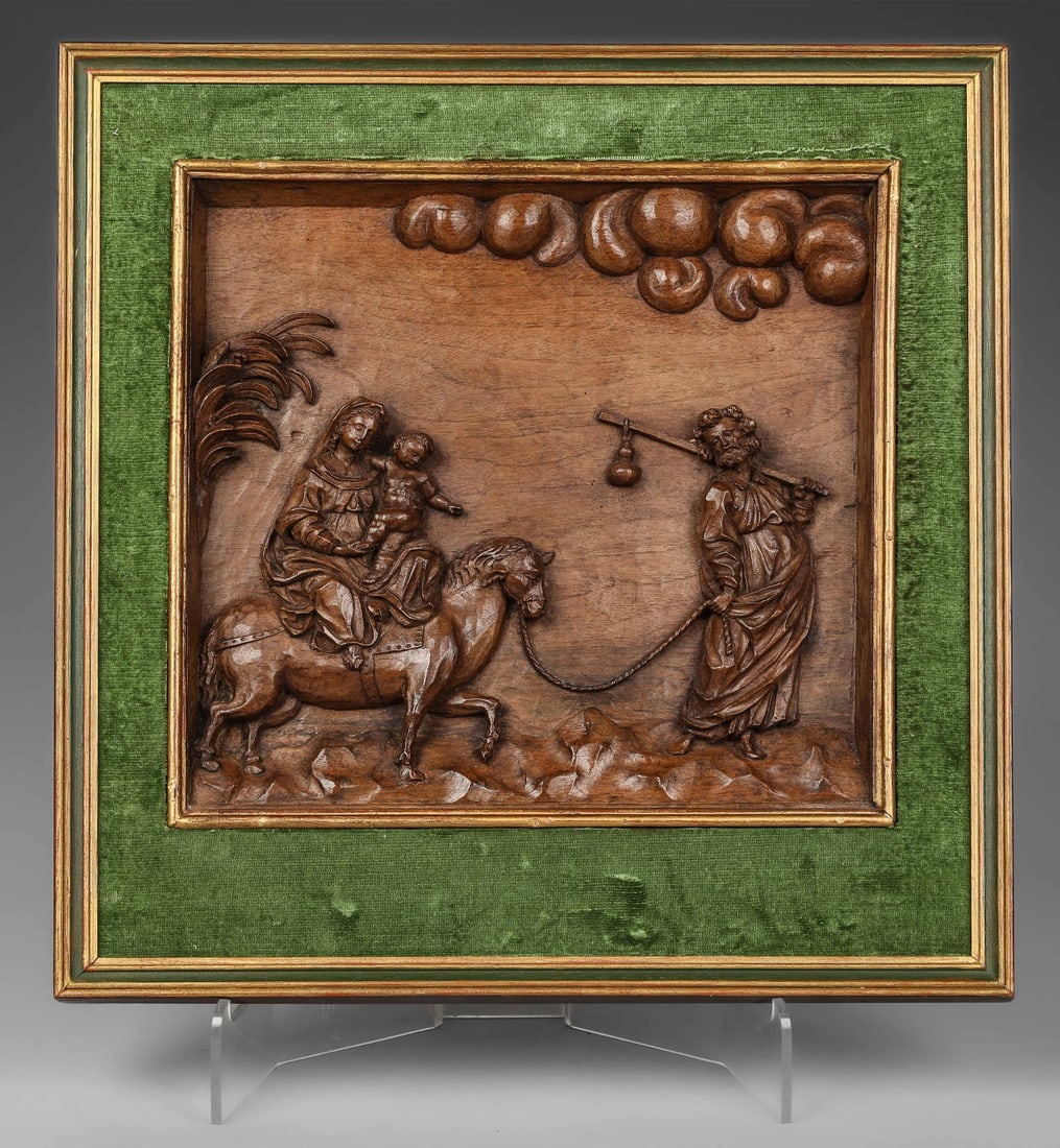 The Flight into Egypt, European School, 17th Century: Walnut panel with relief carving, in a green velvet-covered frame with gilt moldings. Measures 34 x 34 cm; framed 49 x 45 cm. Panel depicting the Flight into Egypt, with Joseph leading the donkey on w