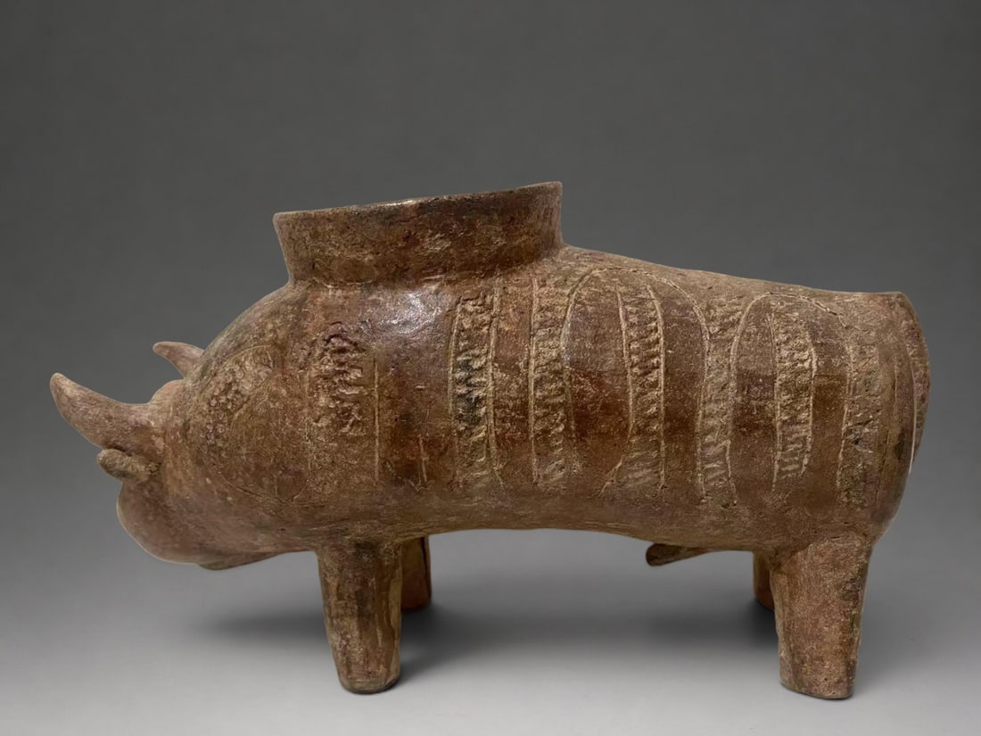 Zoomorphic container in the shape of a bovid, Vietnamese culture, 25th - 15th century BC. c.: Modeled terracotta with incised decoration. Measures 15 x 27 cm. Zoomorphic vessel supported on four legs, with an elongated body and a schematic head featuring protruding horns. The upper part has a 