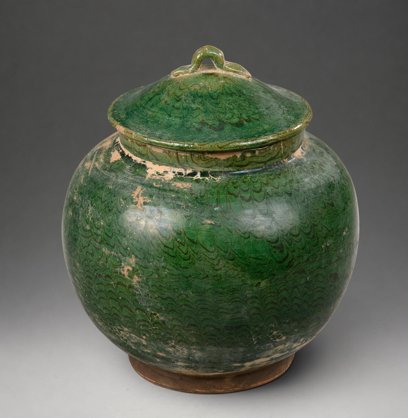 Covered globular vessel, Tang dynasty, 7th-10th century: Green glazed terracotta with dark undertones. Measures 20 cm in height. Globular vessel with a conical lid topped by a small handle. The surface is covered with green glaze featuring wavy decoration i