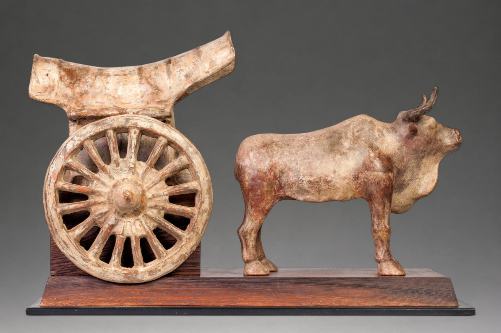 Buffalo chariot, Wei dynasty, 4th - 6th century: Terracotta with traces of polychromy. Dimensions of the piece on its base: 50 x 22 x 14 cm. The composition consists of a standing buffalo next to a chariot with a large radial wheel and a raised, ope
