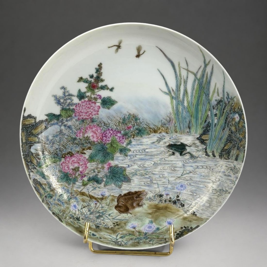 Chinese plate signed - Ming Guo, 20th century: Pink glazed porcelain. Measures 20.5 cm in diameter. Plate decorated with a lakeside landscape populated by frogs and dragonflies among reeds, flowers, and riparian vegetation, painted in delicately t