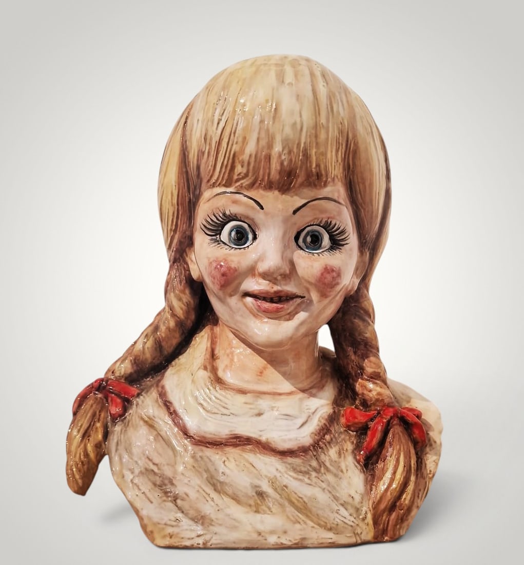 Donno Donno - Busto di ragazza (2017): Glazed ceramic. Dimensions: 30 x 27 x 16 cm. This contemporary sculpture, with its intense expressiveness, depicts the bust of a young woman with a frontal gaze and large, prominent eyes—a distincti