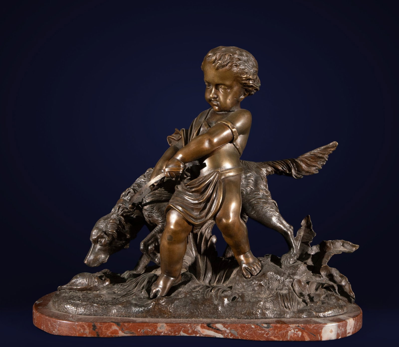 Sculpture of a boy hunter with a bird, Signed, French School, 19th Century: Patinated bronze with a veined marble base. Dimensions: 36 x 44 x 18 cm. This allegorical and naturalistic sculpture depicts a semi-nude child in a dynamic pose, holding a fallen bird while standing o
