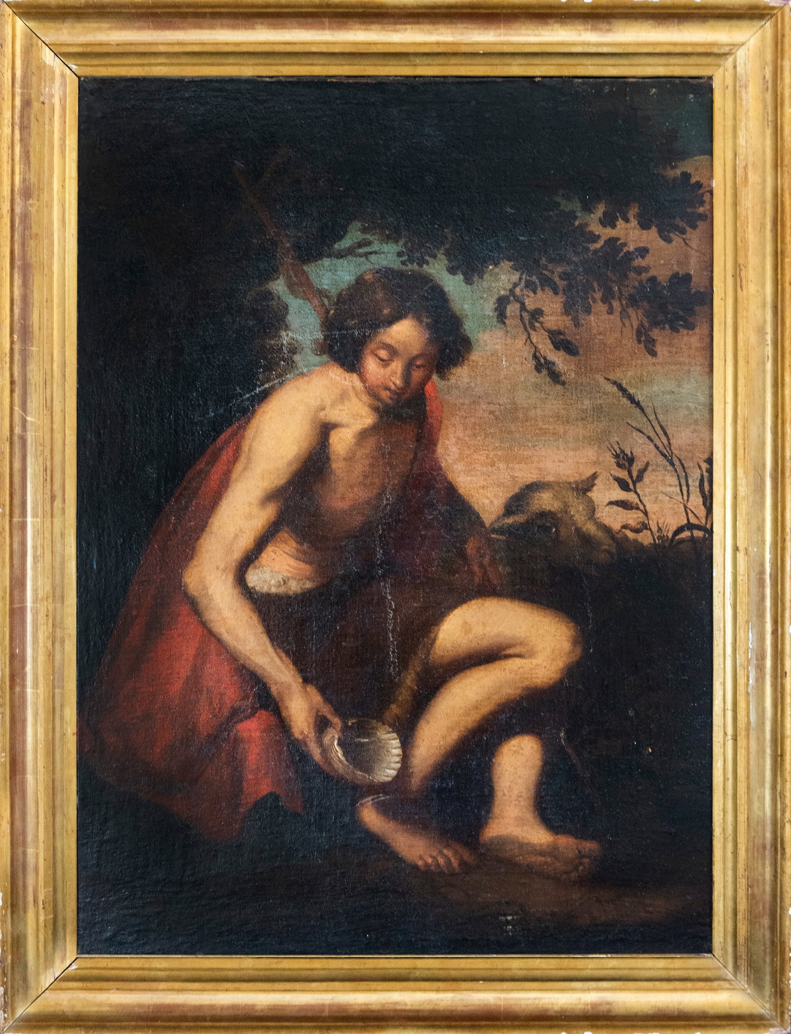Saint John the Baptist in the Desert, Spanish School, 17th Century: Oil on canvas. Dimensions: 86 x 60 cm; framed 100 x 74 cm. Religious scene depicting a young Saint John the Baptist seated in a somber landscape, accompanied by the symbolic lamb and holding a baptism