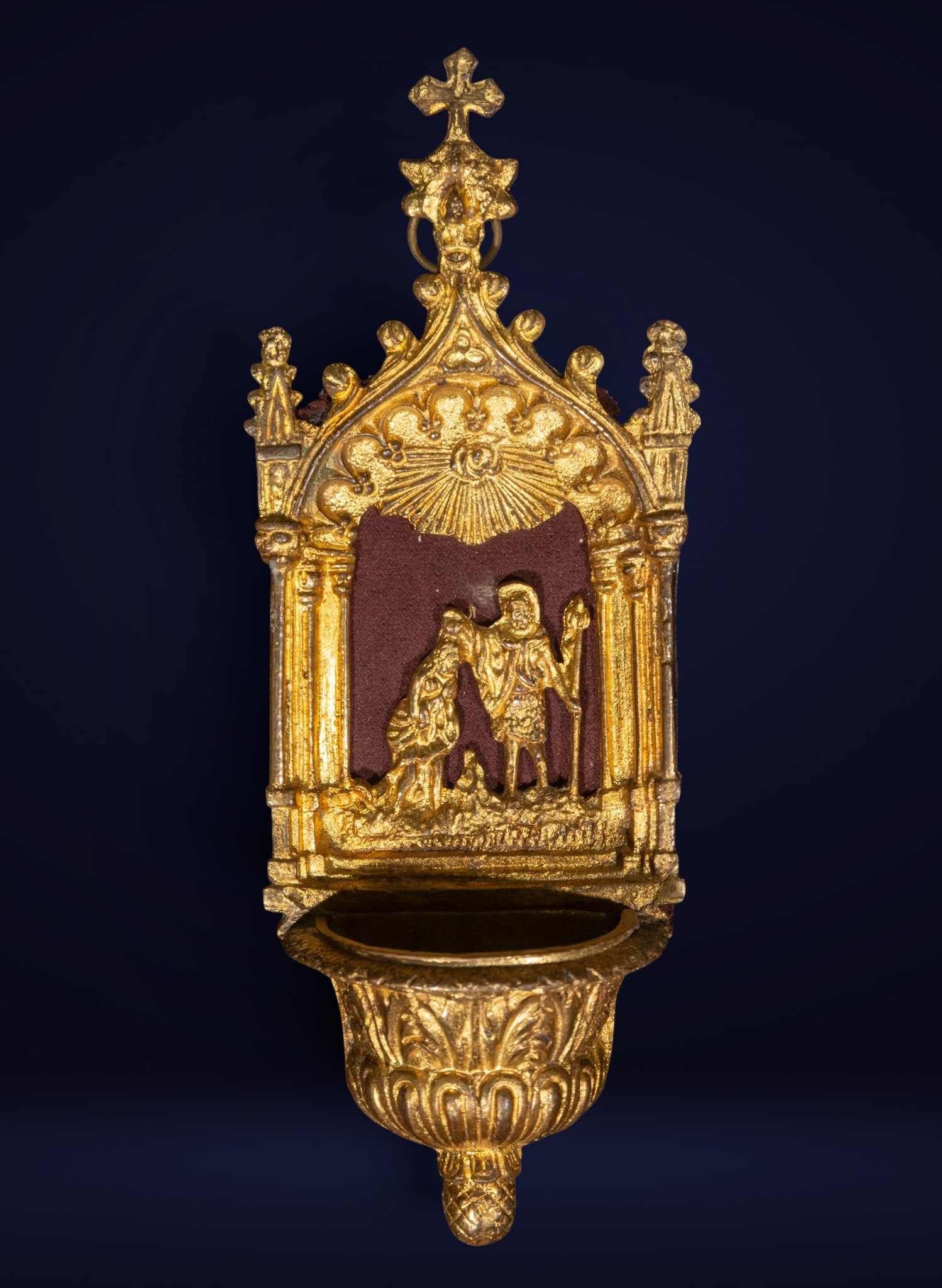 Gilded bronze holy water font, Neo-Gothic School, 19th century: Cast gilt bronze. Dimensions: 20 x 8 x 4 cm. Gilt bronze holy water font with a Neo-Gothic architectural structure and a central scene of Saint John the Baptist in relief. The composition features poi