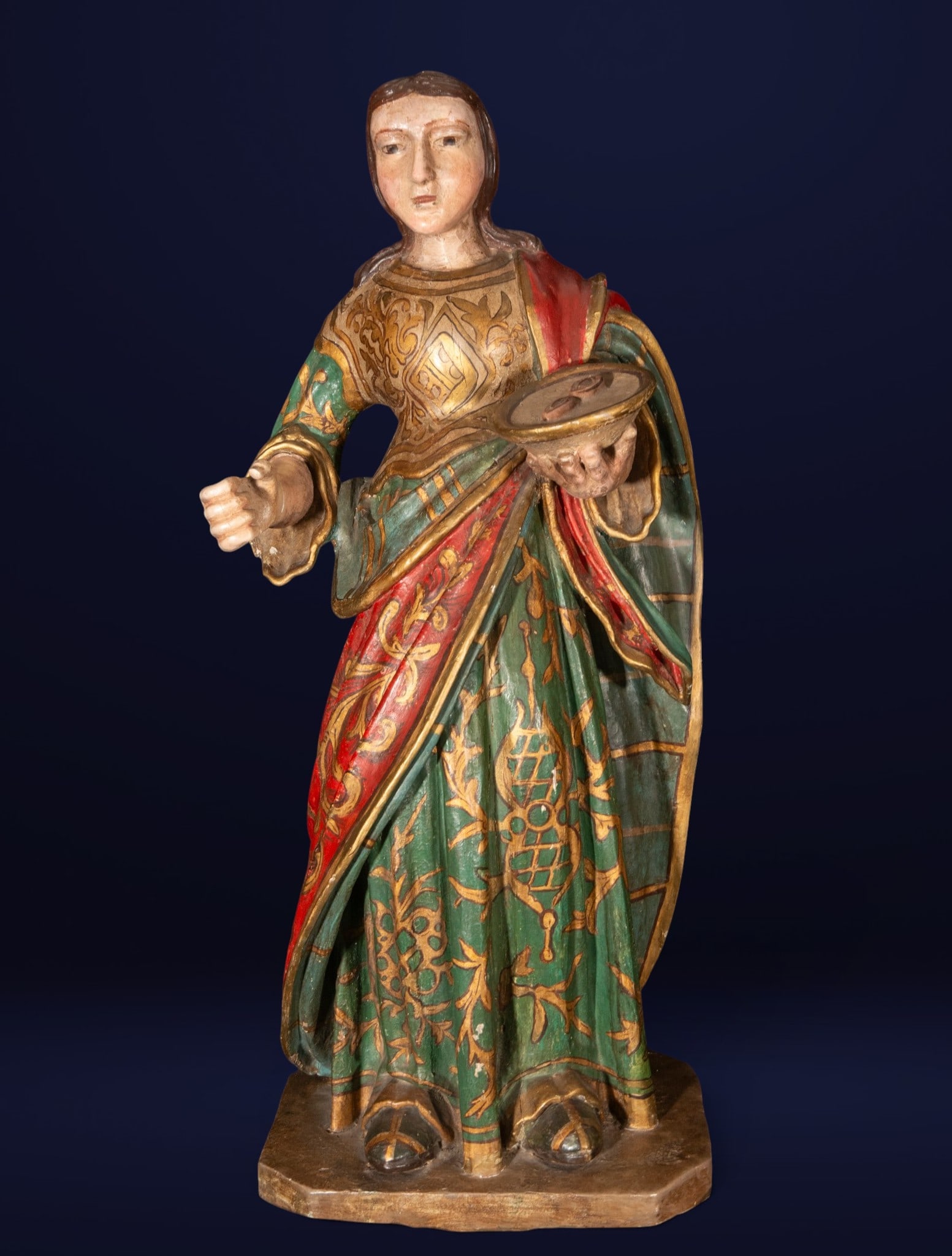 Saint Lucy, Spanish School, 17th Century: Carved, polychromed, and gilded wood. Dimensions: 74 x 34 x 25 cm. Sculpture of Saint Lucy depicted standing with an elegant frontal pose, holding in one hand the tray containing her eyes, an iconogra