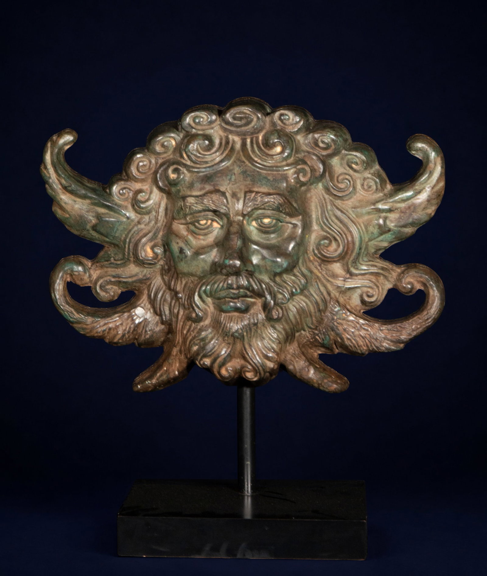 Large Bronze Grand Tour Mask of Mercurius, 20th century: Patinated bronze. Measures 49 x 45 x 17 cm. This ornamental sculpture of mythological inspiration depicts the face of Mercury with side wings and exuberant, flowing hair rendered in intricate scrolls.
