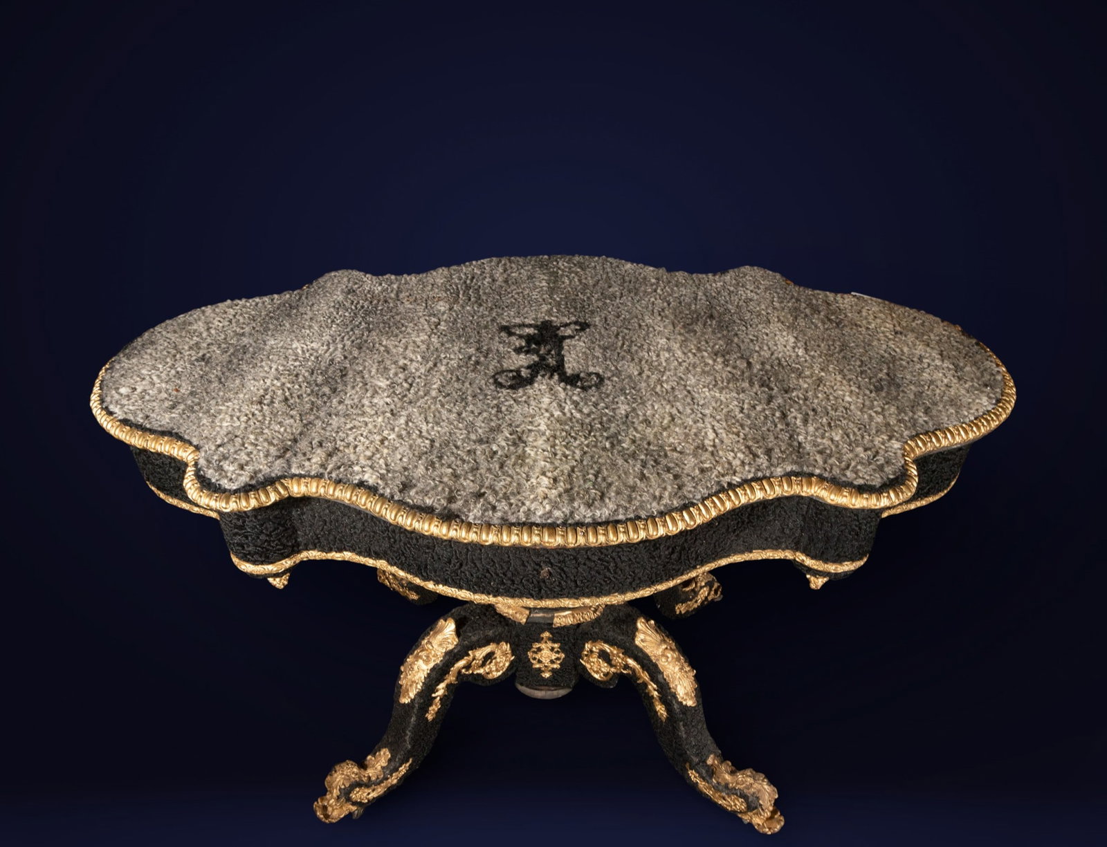 Russian table in astrakhan with central shield. Russian school. 19th century.: Wood covered in astrakhan leather with mercury-gilt bronze mounts. Measures 74 x 126 cm. An extraordinary work table of Russian origin, with a top and aprons covered in astrakhan leather, creating a s