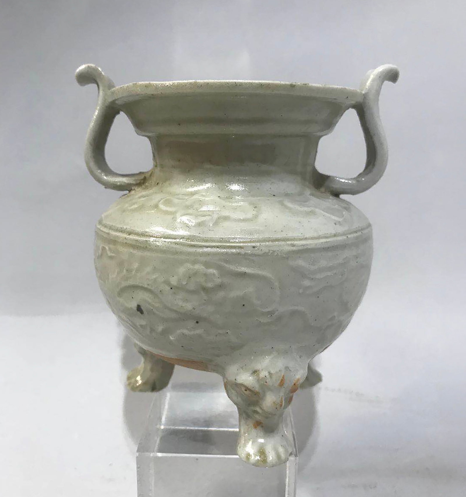 Pot-bellied tripod perfume burner with a large mouth and two side handles on the neck: Molded with chimeric heads on the foot and dragons on the body, in fine porcelain stoneware with a monochrome blue celadon glaze. China. Song Dynasty. 960 to 1279. Height 11 cm x diameter 8 cm. Lot in
