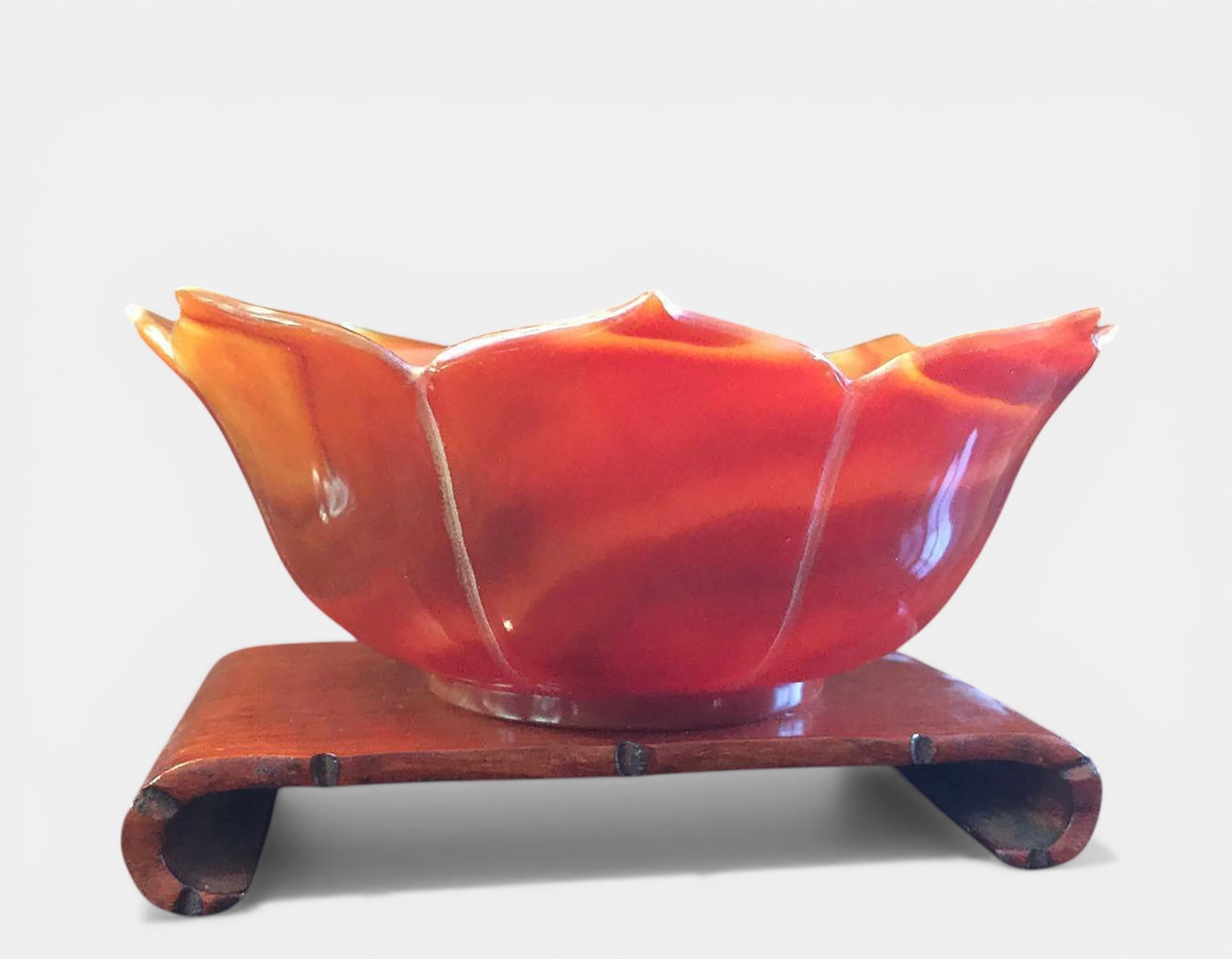 Lotus flower shaped cup carved from natural orange-red agate: Carved from a natural reddish-orange carnelian agate, following the undulating, veined contours of an open lotus petal, with a high polish that enhances the translucency and richness of the agate's mi