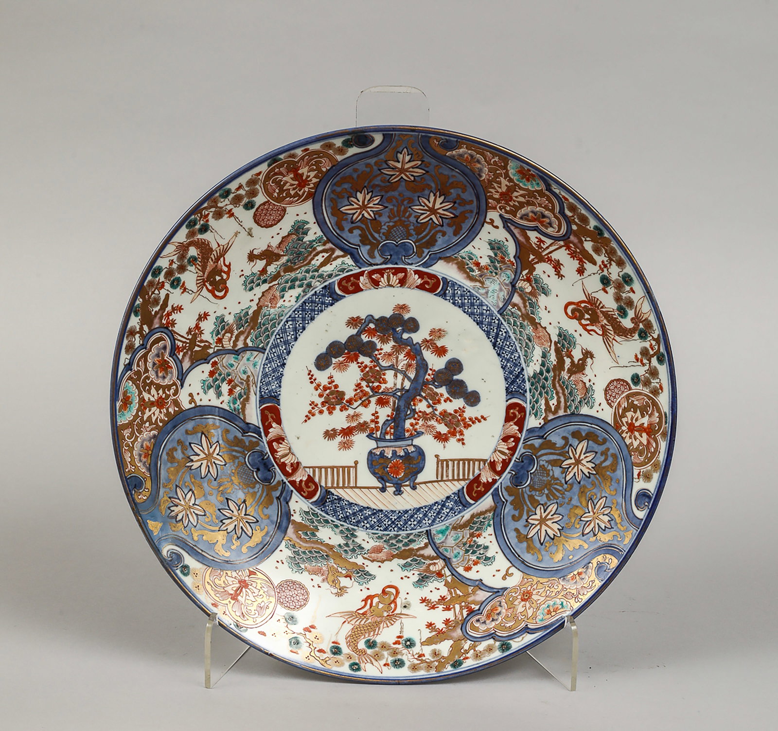 Imari porcelain plate with polychrome decoration of flowering bonsai: Polychrome decoration in blue, red, and gold, with a central motif of a flowering bonsai in a vase on a terrace, surrounded by reserves with floral and vegetal motifs on a background of scrolls and st