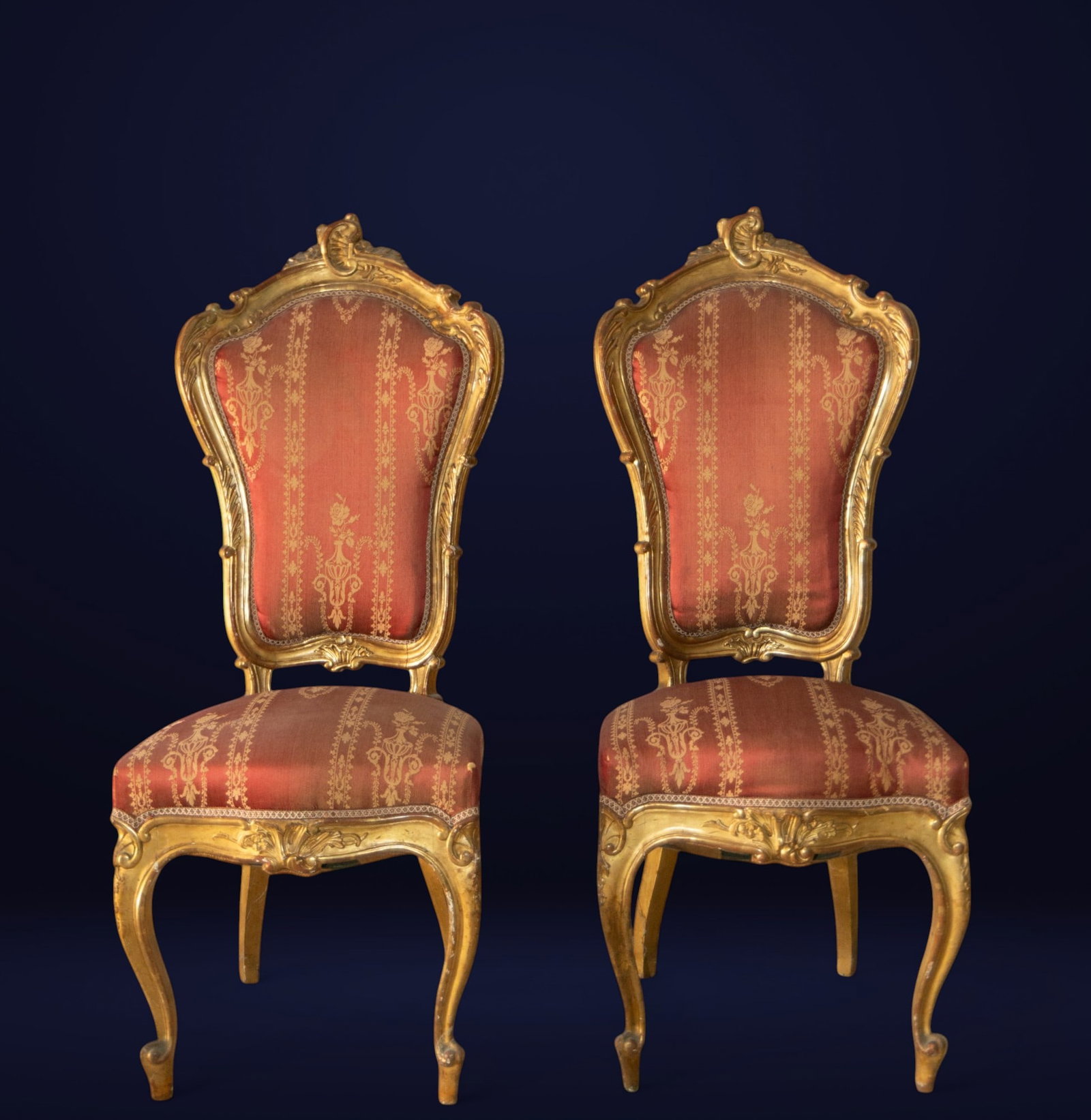Pair of gilded chairs with original upholstery. European School. Late 19th century.: Carved and gilded wood with textile upholstery. Dimensions: 115 x 46 x 53 cm. Set of two high-backed chairs with curvilinear shapes and lavish Rococo carvings on the gilded frame. The backrests and se