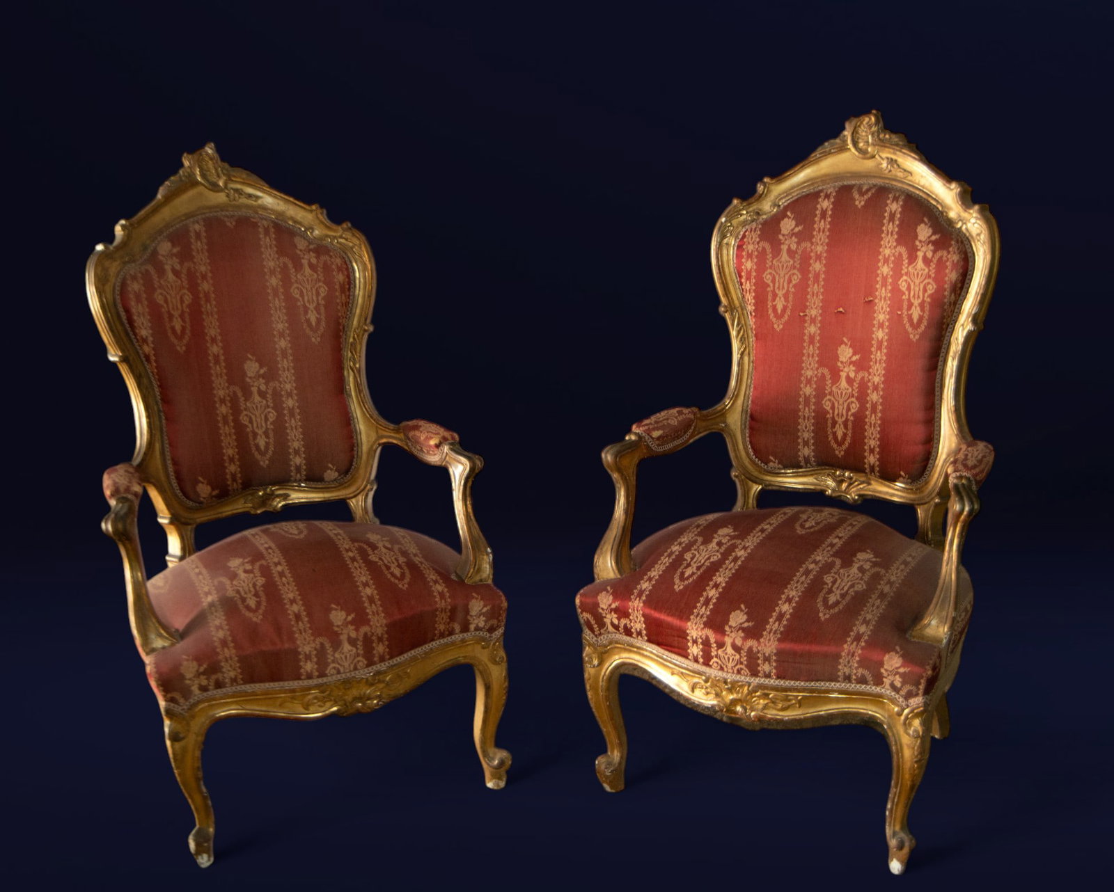 Pair of gilded armchairs with arms and original upholstery. European School. Late 19th century.: Carved and gilded wood with textile upholstery. Dimensions: 120 x 69 cm. Set of two high-backed armchairs with molded arms, featuring a gilded frame and Rococo carving that emphasizes scrolls and flor