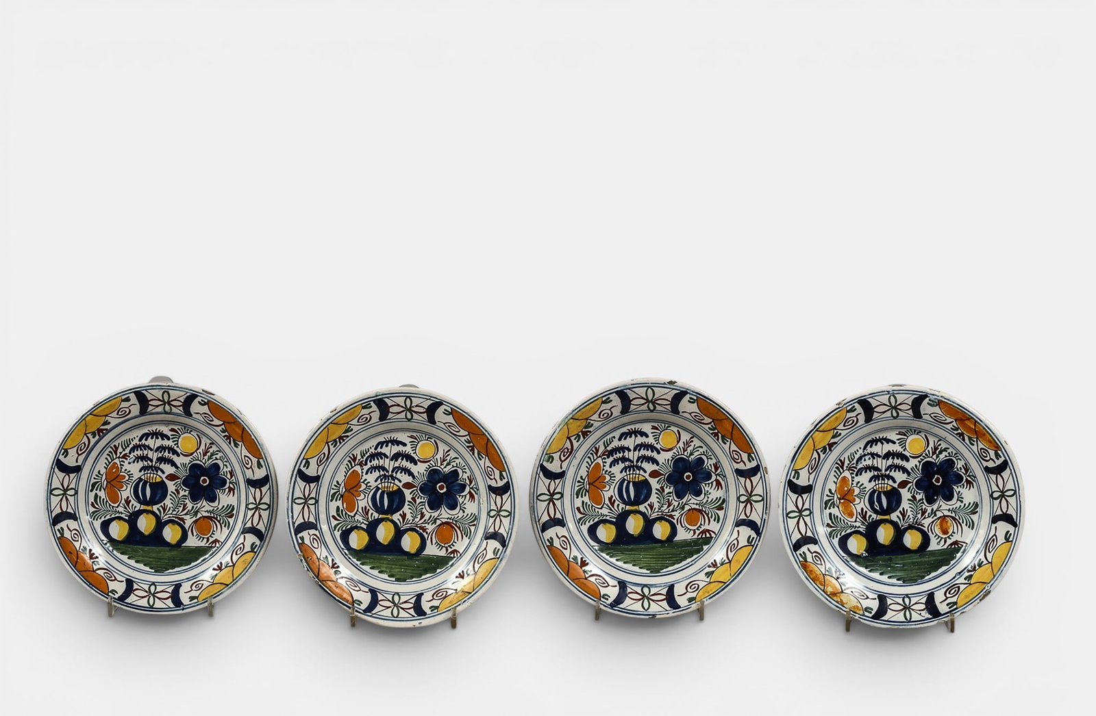 Set of four earthenware plates with high-fire polychrome decoration: Featuring a stylized bouquet motif in blue, yellow, and orange, surrounded by foliage and flowers, and a wing decorated with geometric and floral designs. The reverse is white enamel, unmarked, with f