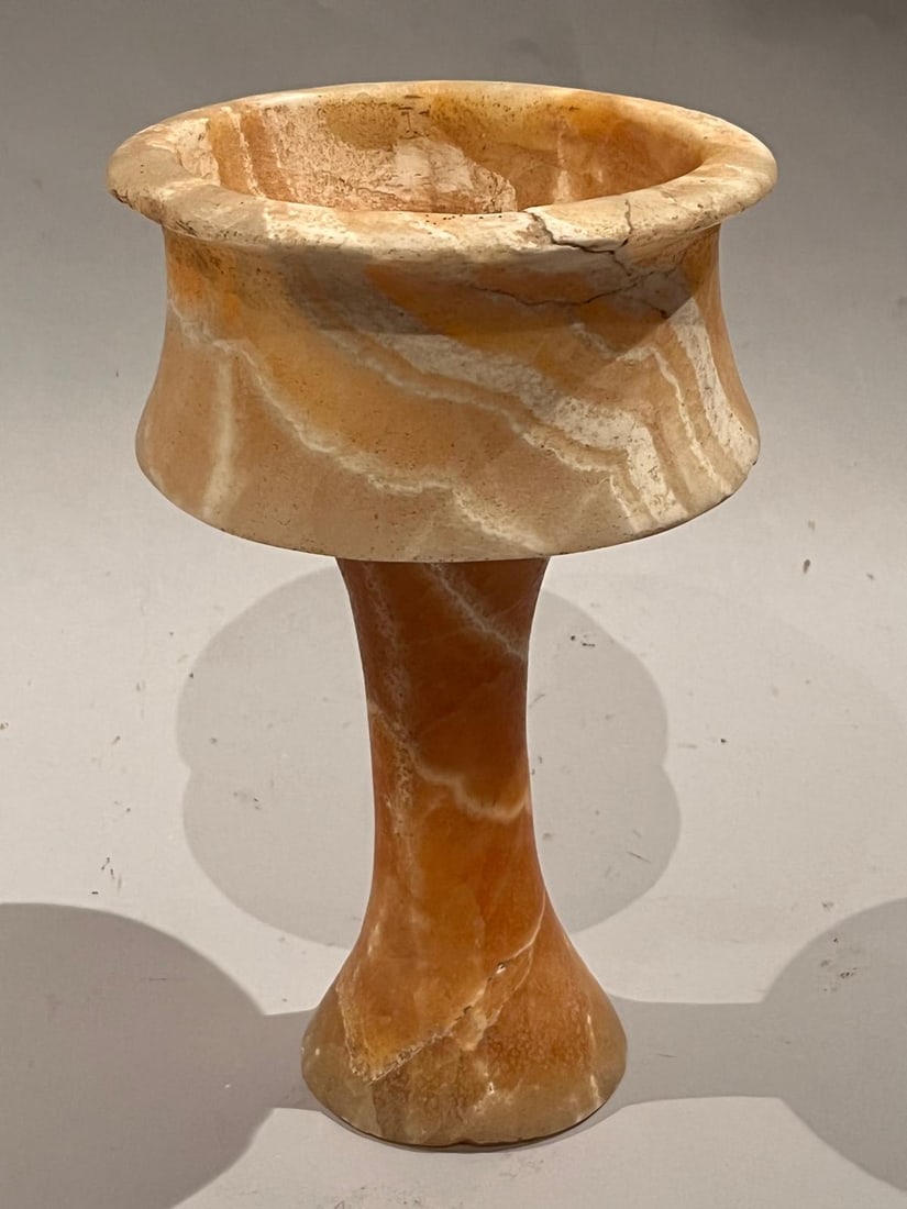 Calcite-alabaster vase carved from a single block, in the shape of a chalice: With a wide, everted mouth, a slightly open belly atop a tall, truncated conical foot ending in a flared base. Beautiful honey-colored patina and white veining. The stone exhibits marked honey-ochre a