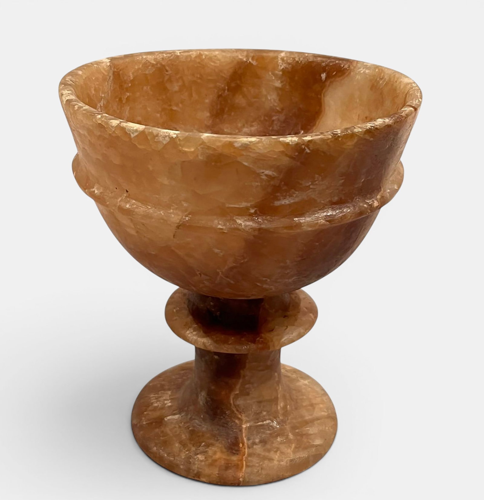 Translucent calcite alabaster cup carved from a single block: Open, truncated cone-shaped vessel with a wide, scalloped rim, resting on a double-torus annular foot and a circular base. The translucent ochre stone displays a warm veining typical of quarries in th