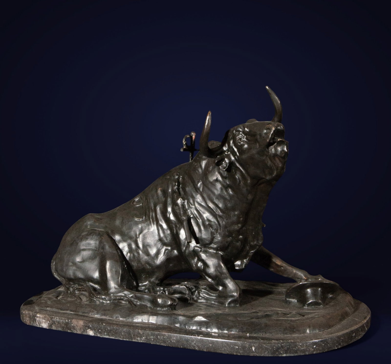 Wounded bull in the arena, European school, 20th century: Bronze. Measures 40 cm x 53 cm x 30 cm. The sculpture depicts a bull collapsed on an oval base, its body leaning to one side and its head raised in a bellowing gesture. Sticks are visible in its back 