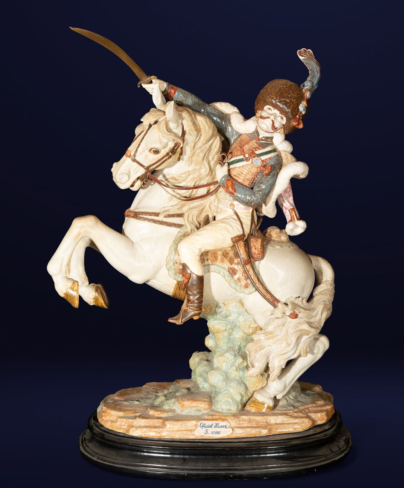 Figure of a Hungarian light cavalry hussar. European school. 20th century.: Polychrome porcelain with gold details and a lacquered wooden base. Measures 86 x 68 x 35 cm. Large-format sculpture depicting a hussar on horseback, brandishing a saber, with a detailed uniform and p