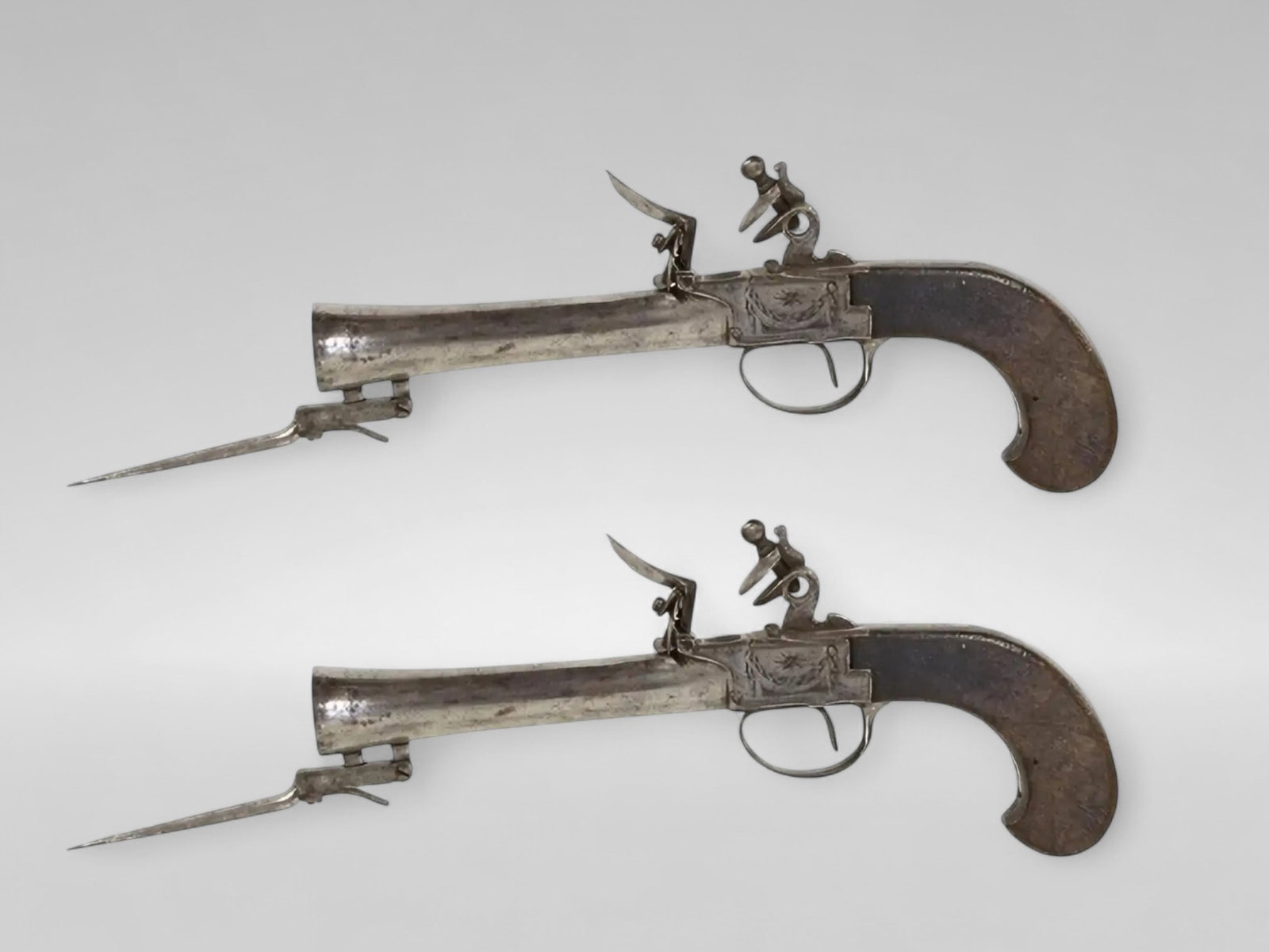 Pair of muzzle-loading travel pistols with flintlock and tilting bayonet, European School, 19th: Iron and wood. Dimensions: 24 cm. Pair of European flintlock travel pistols, made in the first half of the 19th century, with a flintlock mechanism and short iron barrels, slightly flared at the muzzl