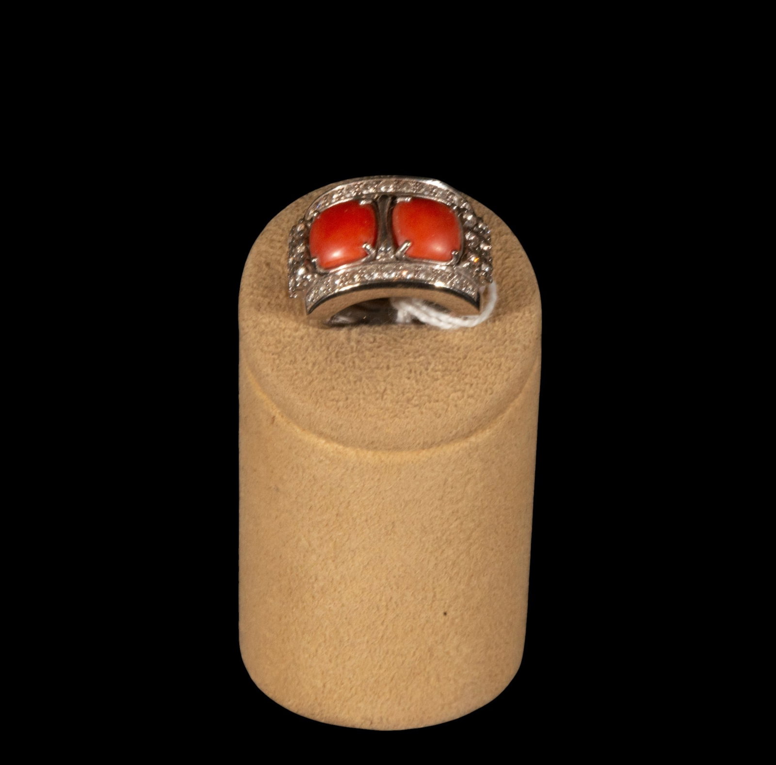 White 18k gold ring with two coral cabochons and diamonds, weight 14.37 grams: A white 18k gold ring with two coral cabochons and diamonds, weighing 14.37 grams. The piece features an open and symmetrical front, dominated by two oval coral cabochons in a pinkish-orange hue, set 