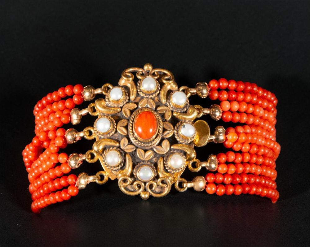 Bracelet made of coral threads and a gold-plated silver clasp with coral cabochon pearls: Coral strand bracelet with a gold-plated silver clasp and coral cabochon pearls. Made up of multiple strands of small coral beads in shades of red and orange, it fastens with a central gold-plated met