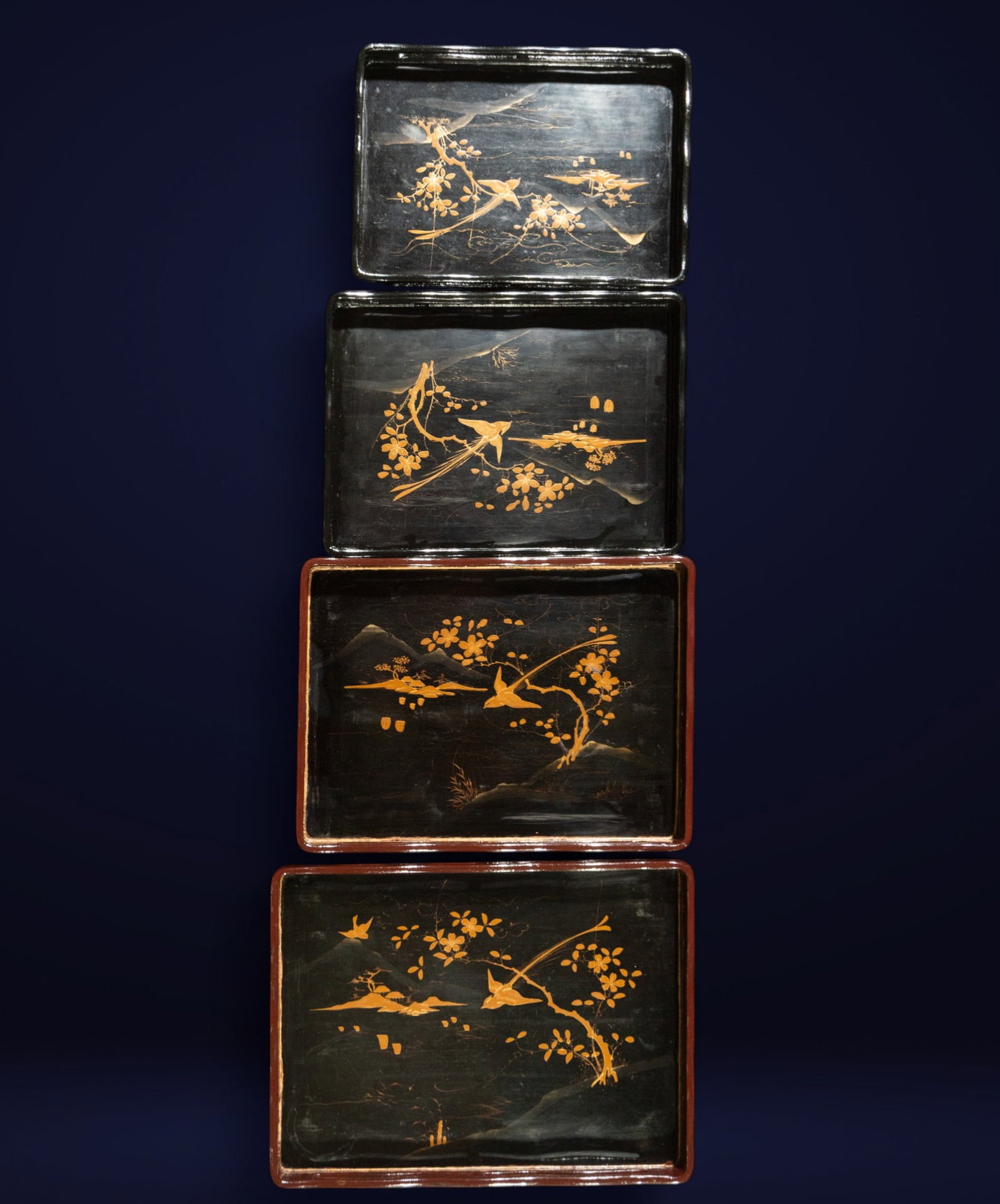 Set of lacquered trays with oriental motifs, Japan, 20th century: Lacquered and gilded wood. Dimensions: Largest: 42 x 30 x 4 cm. Smallest: 35 x 22 x 3 cm. A set of four rectangular trays with a black background and gilded plant and bird decoration, possibly made us